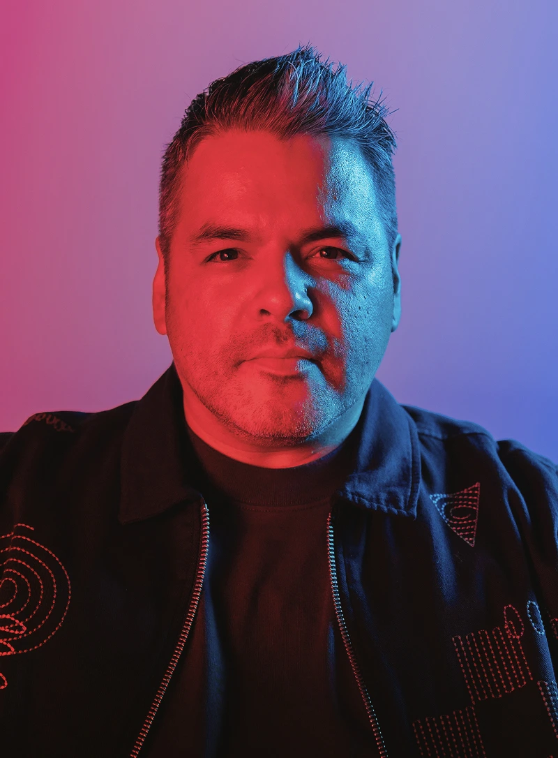 Portrait of Ricky Ratcliff illuminated by red and blue lighting against a gradient background.