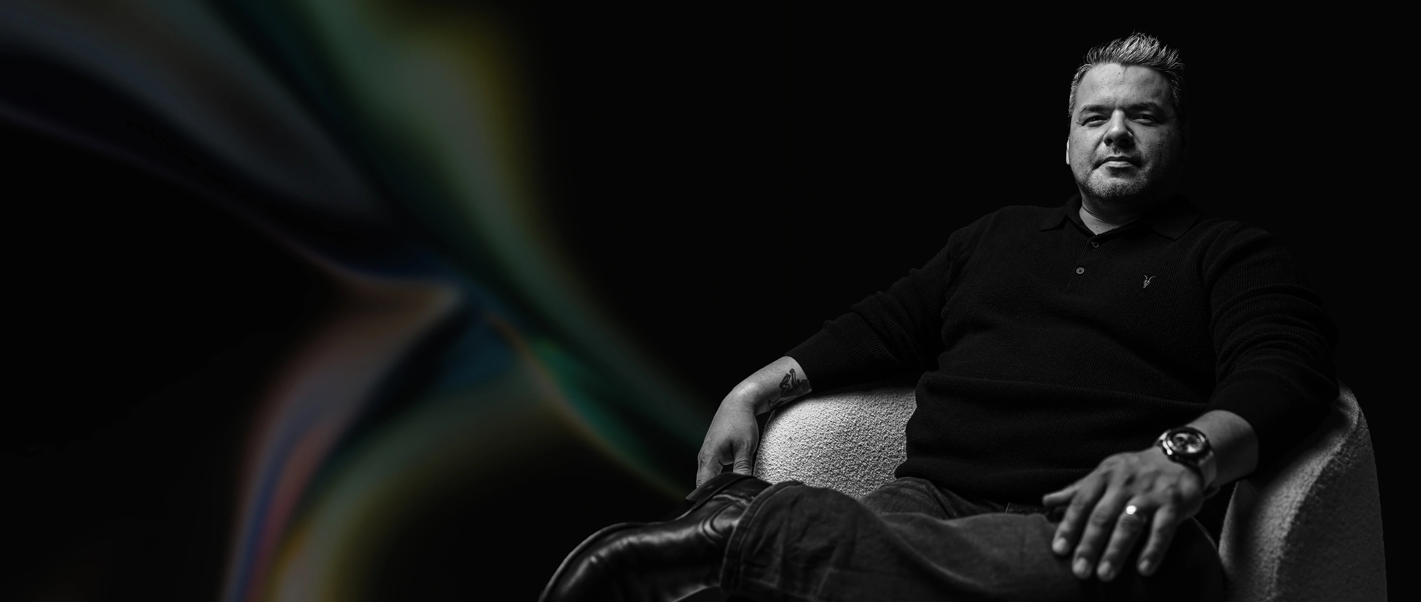 Ricky Ratcliff sitting on a textured chair against a dark abstract background.