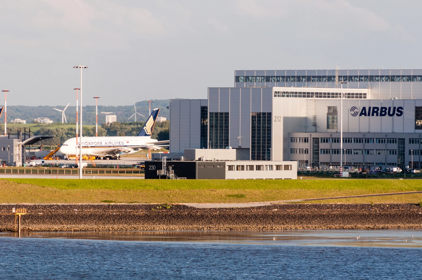 Flughafengebäude von Airbus mit einem geparkten Singapore Airlines Flugzeug und Windrädern im Hintergrund.