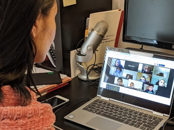 Person participating in an online video conference on a laptop with multiple participants visible on screen.