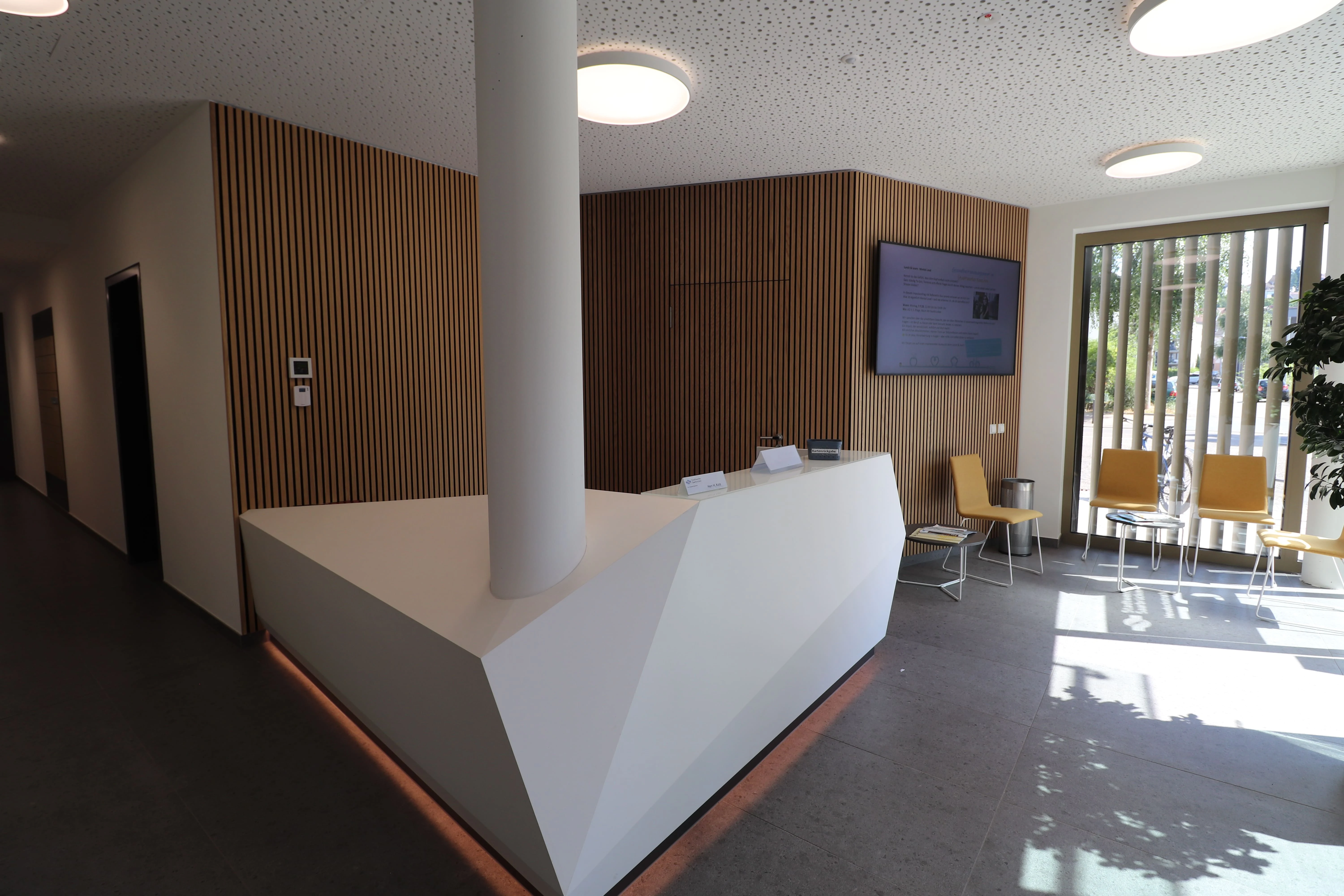 Empfang der Stadtwerke Saarbrücken mit weißer Empfangstheke und Infodisplay an einer Holzlamellenwand