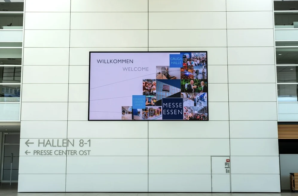 Großer Welcome Screen der Messe Essen mit Willkommensgruß und Veranstaltungsbildern über der Wegweisung zu den Hallen