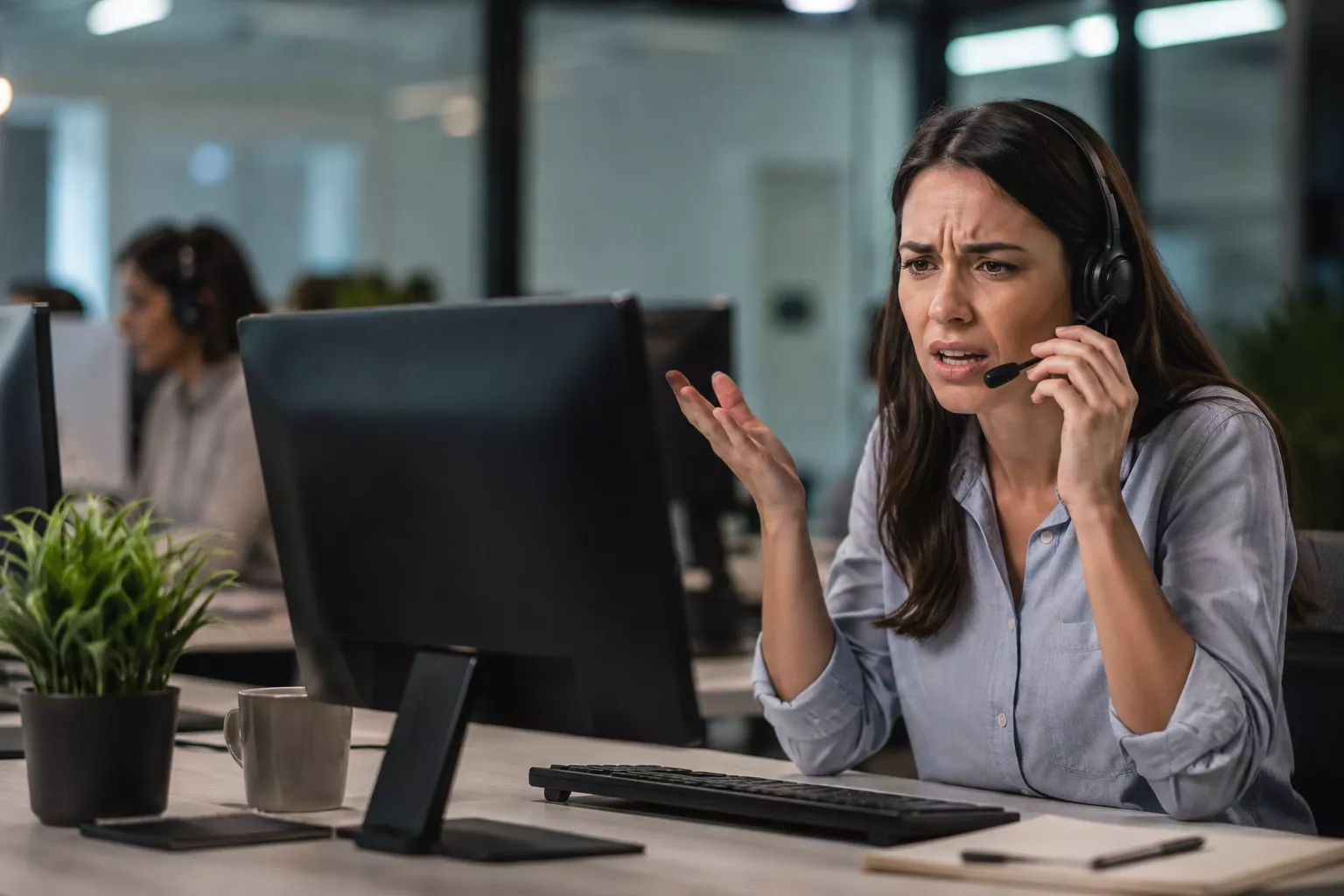 Frustrated customer service representative handling a difficult phone call in a modern office, illustrating customer support challenges and AI call handling solutions.