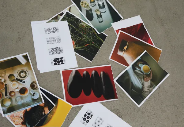 Scattered printed photos on a gray surface showing various subjects including coffee cups, abstract patterns, plants, shoes, and a person holding a cup.