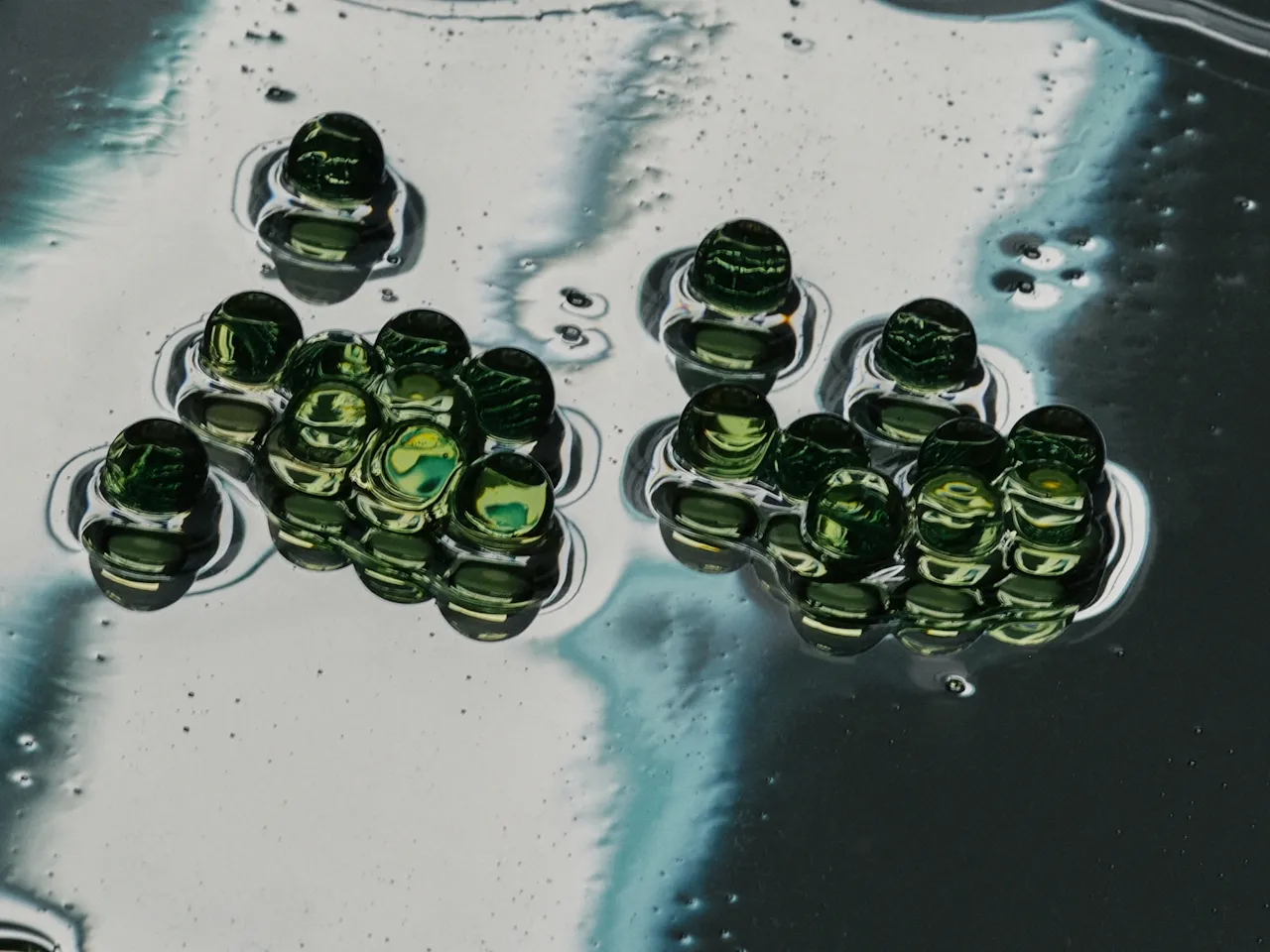 Clusters of green glass marbles on a reflective, liquid-like surface.