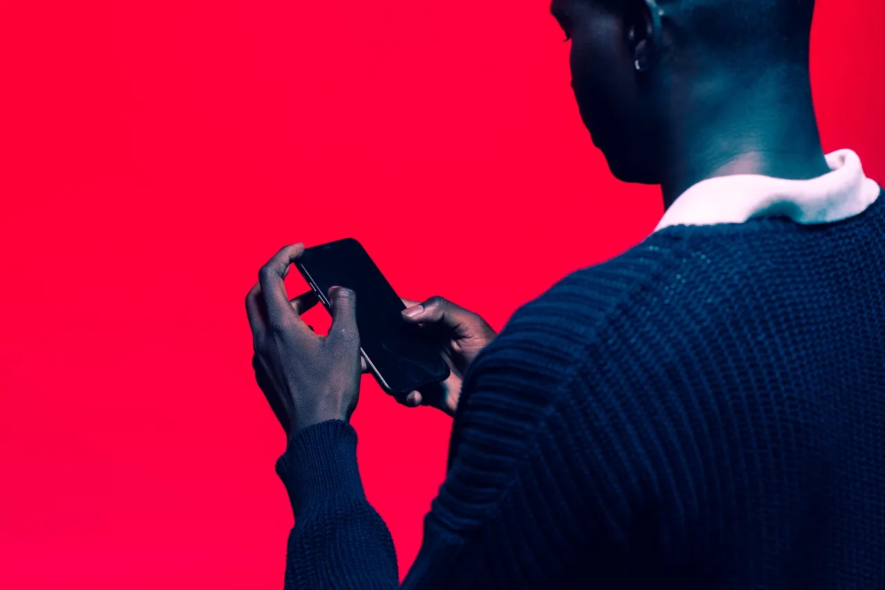 Person wearing a dark sweater holding and looking at a smartphone against a bright red background.