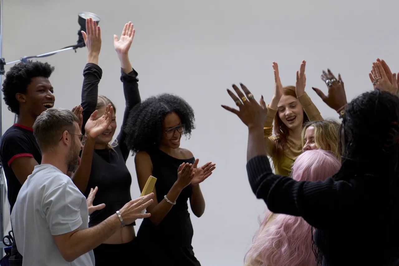 Diverse group of people smiling and raising their hands in celebration in a studio setting.