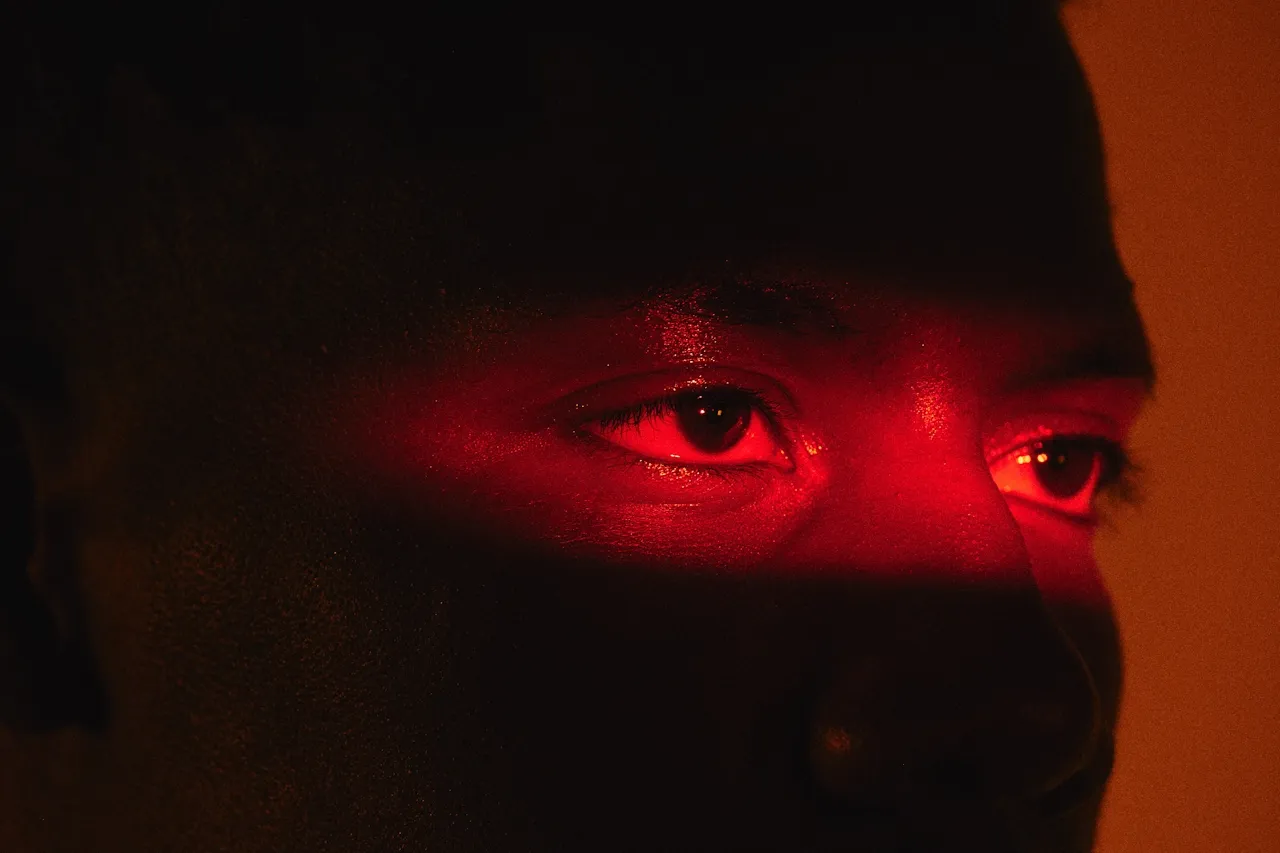 Close-up of a person's eyes illuminated by red light in a dark environment.