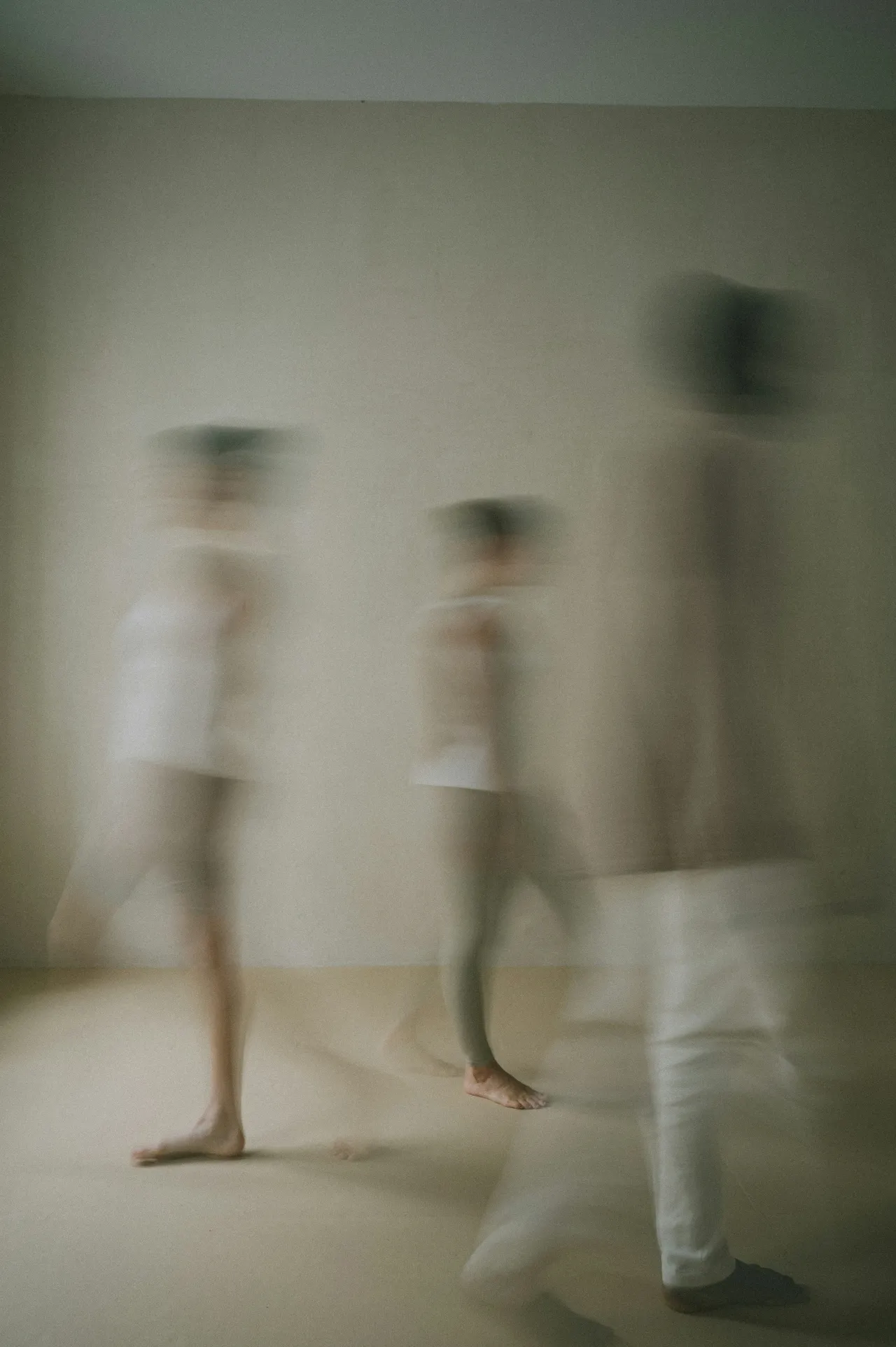Blurred motion image of three people walking barefoot across a neutral-toned room.