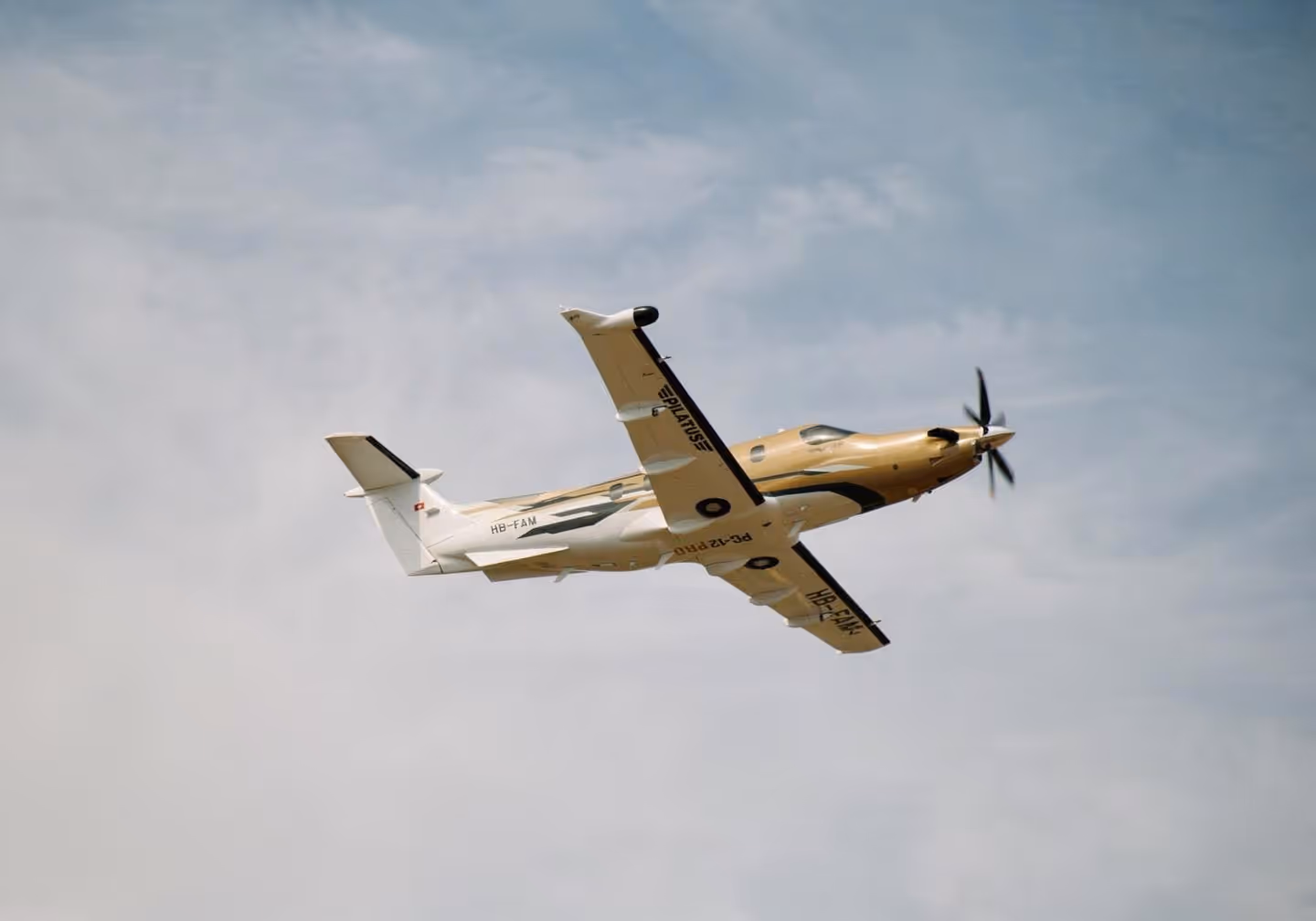 Single-engine propeller airplane flying against a cloudy blue sky.