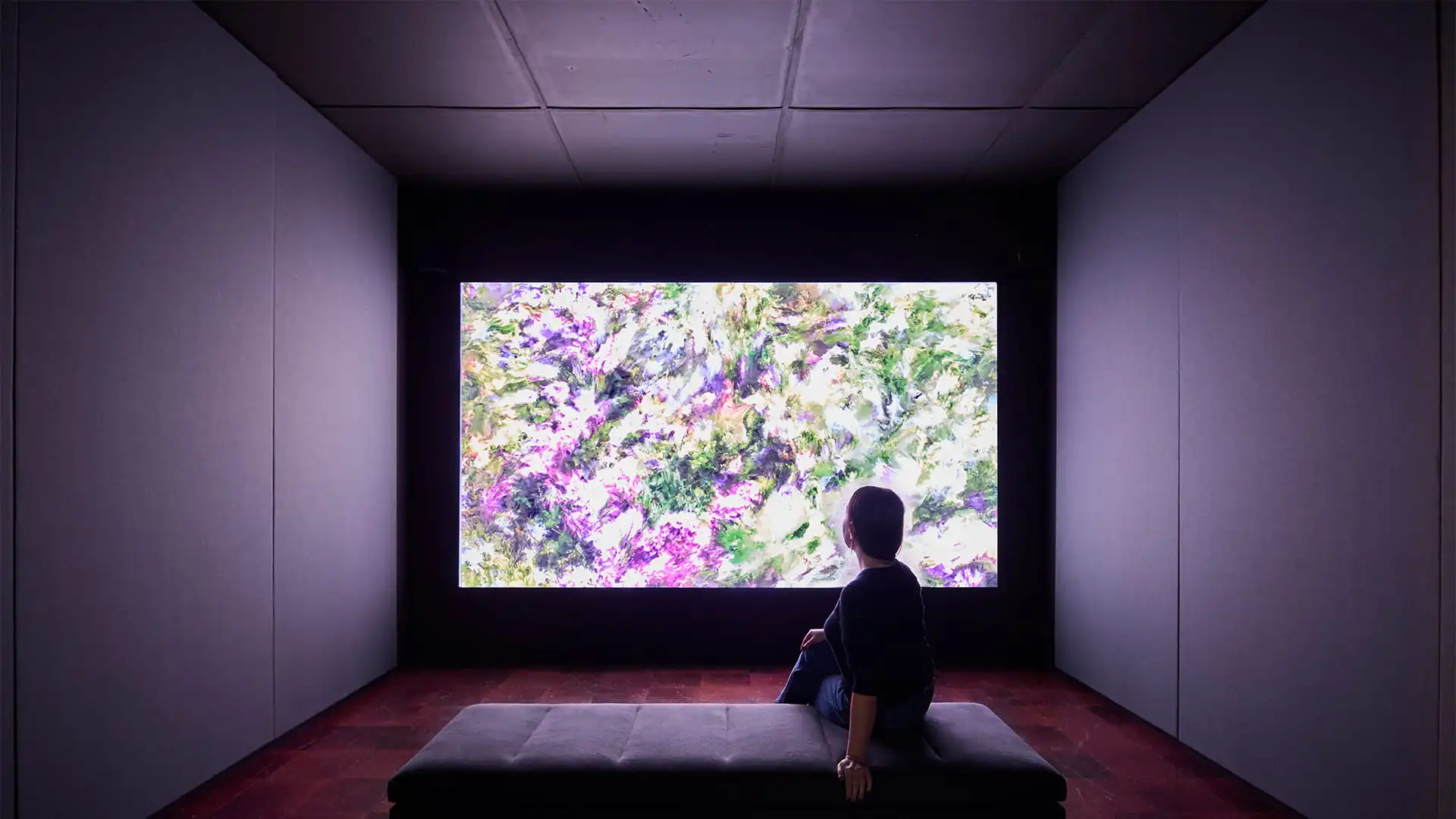Large LED screen displaying a colorful abstract swirl pattern mounted on a black modular panel system against a dark background.
