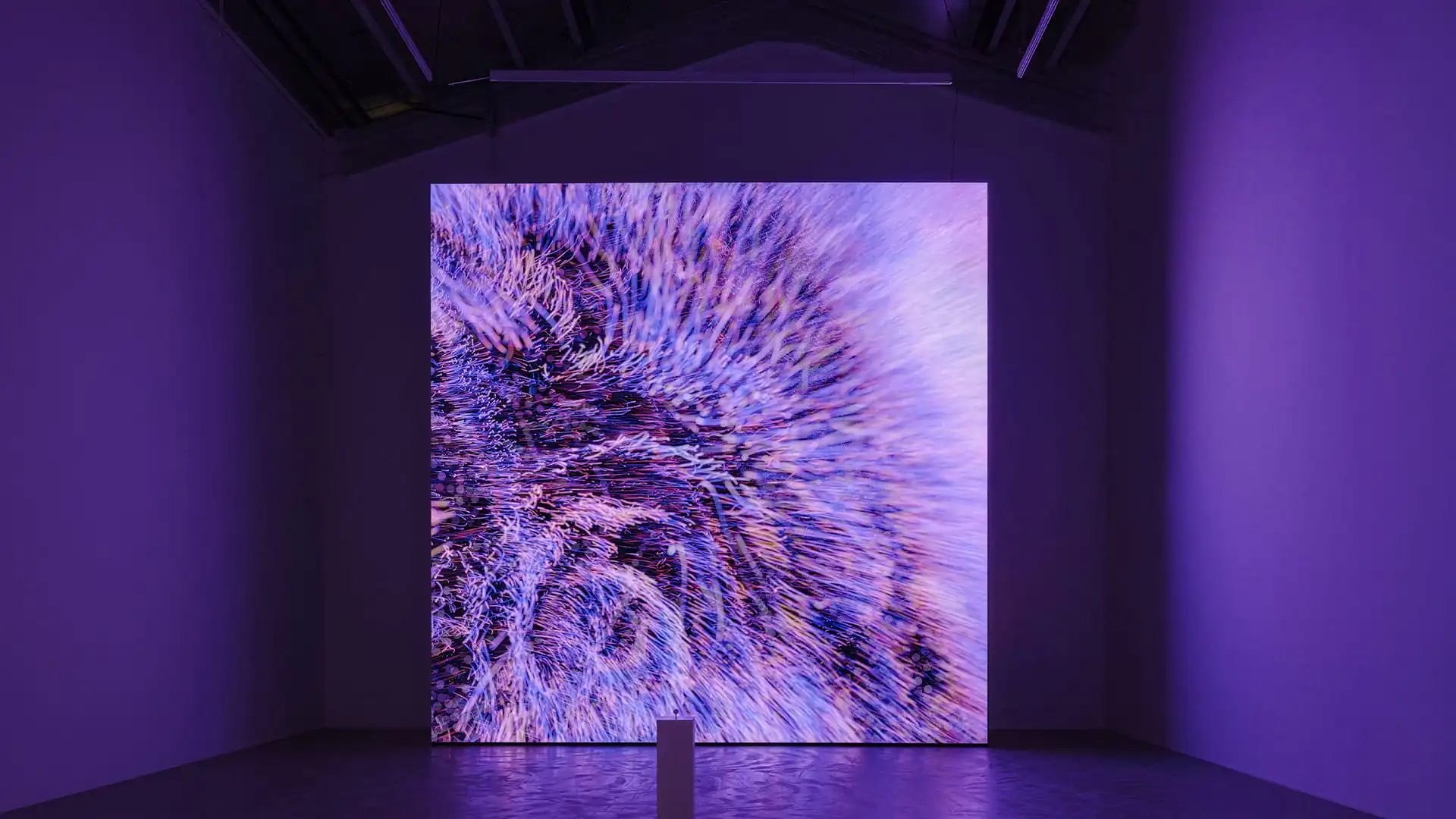 Large LED screen displaying a colorful abstract swirl pattern mounted on a black modular panel system against a dark background.