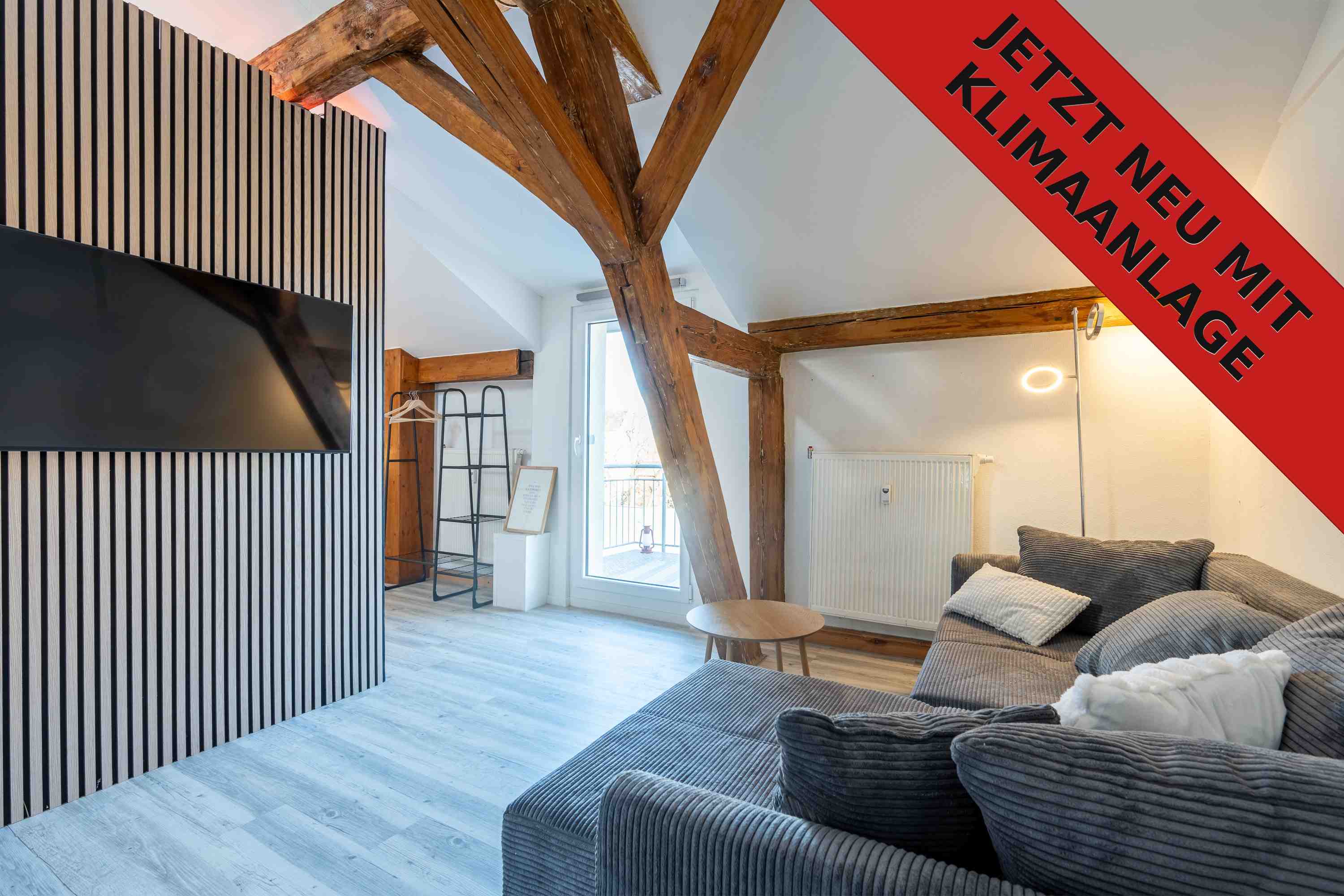 Foto vom Wohnzimmer in der Dachgeschosswohnung mit Fernseher und grauem Sofa