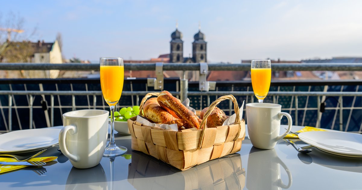 Frühstück auf dem Balkon einer Ferienwohnung in Bamberg mit Brezen, Croissants und Orangensaft, im Hintergrund die Türme von St. Gangolf