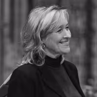 Black and white portrait of a smiling woman with short light hair, wearing a dark turtleneck and blazer, looking to the right.