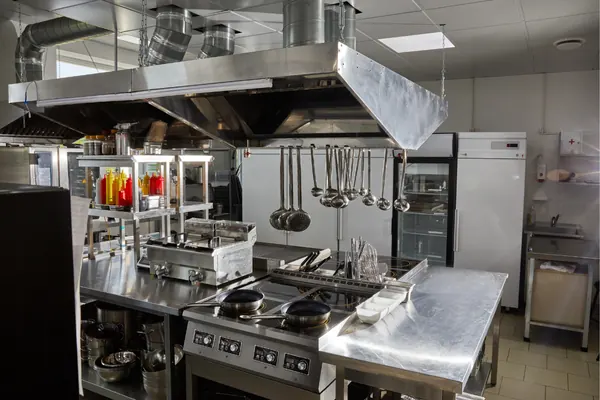 Stainless steel commercial kitchen with cooking equipment and ventilation hood.