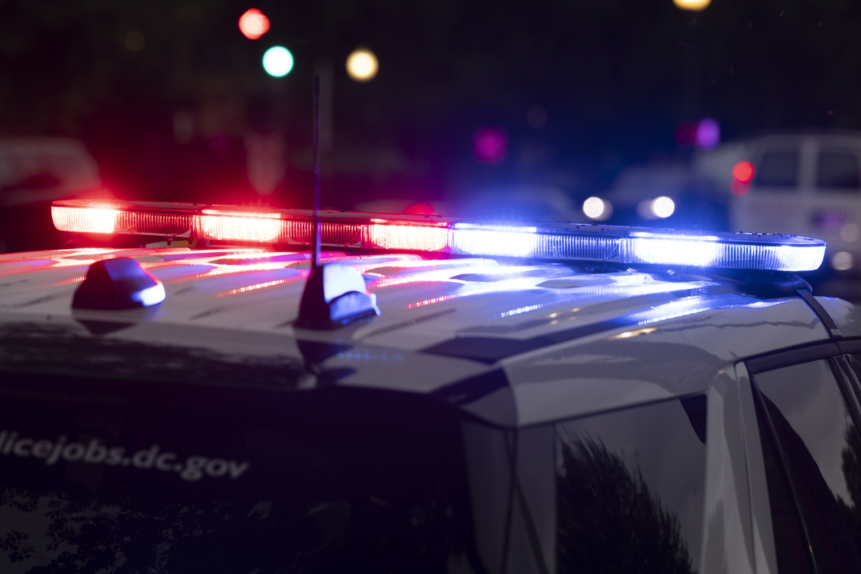 Red and blue emergency lights flashing on top of a police car at night.
