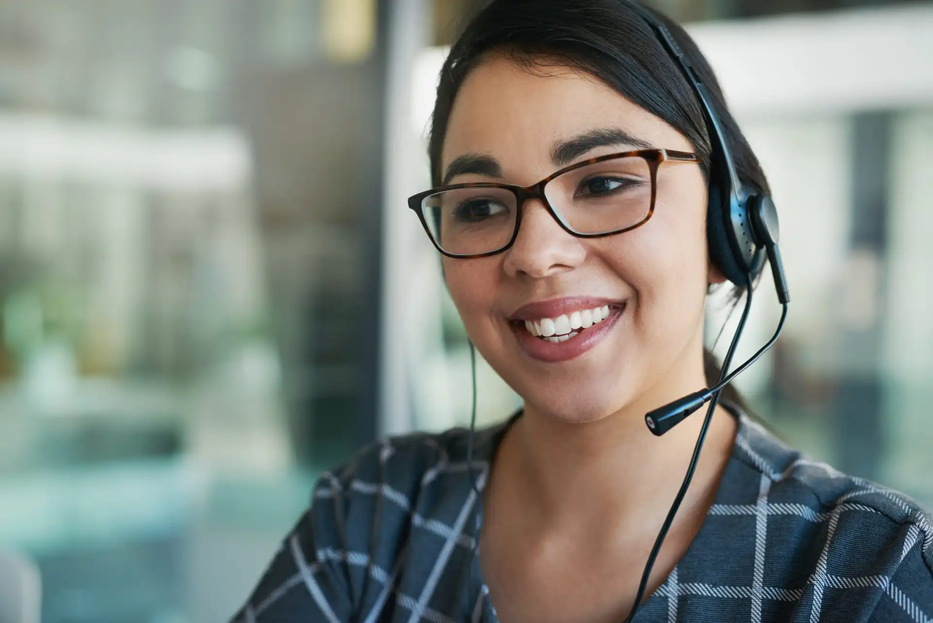 Smiling woman wearing glasses and a headset with a microphone in an office setting.
