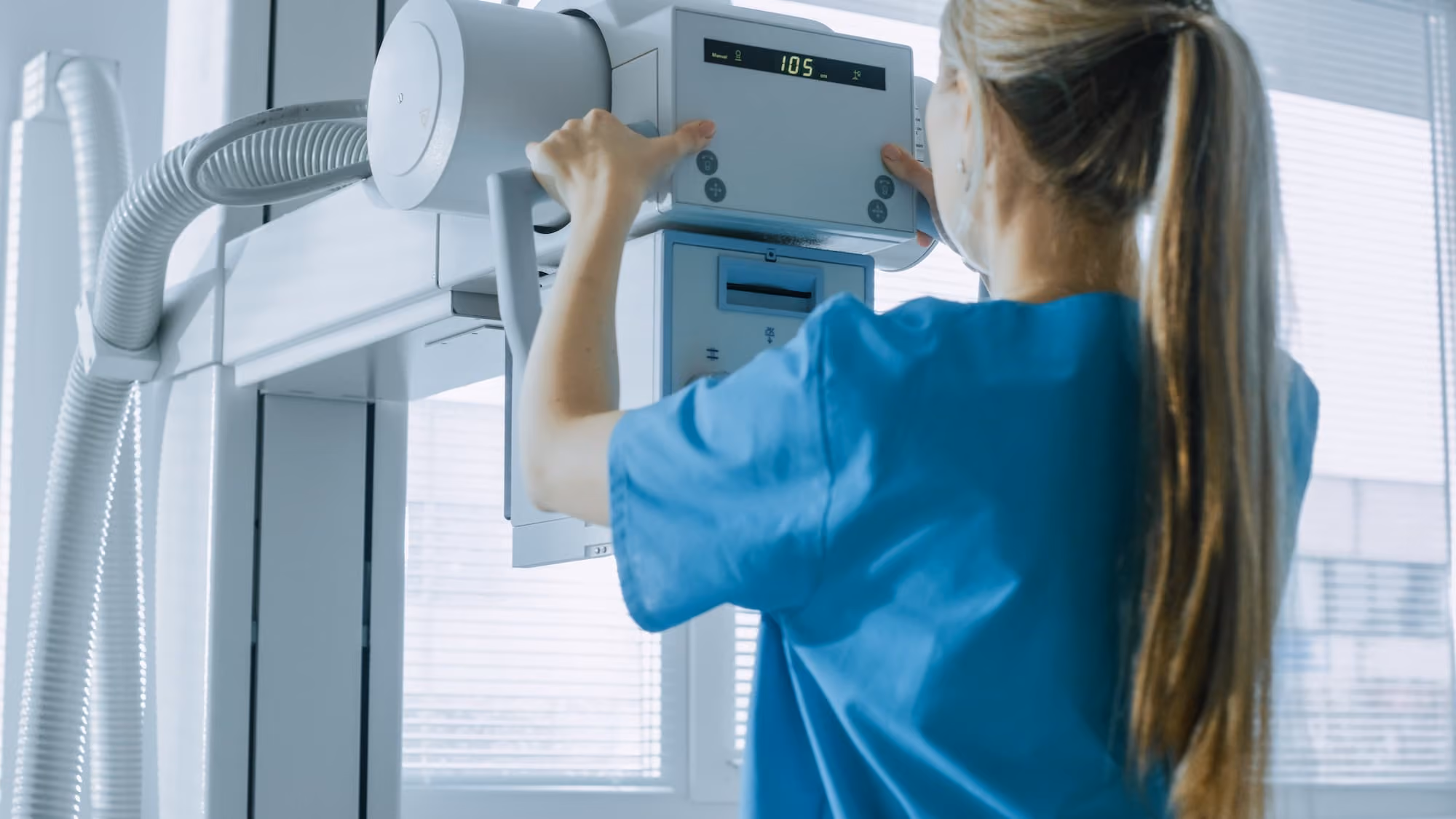 Medical professional in blue scrubs adjusting a digital display on radiology equipment.