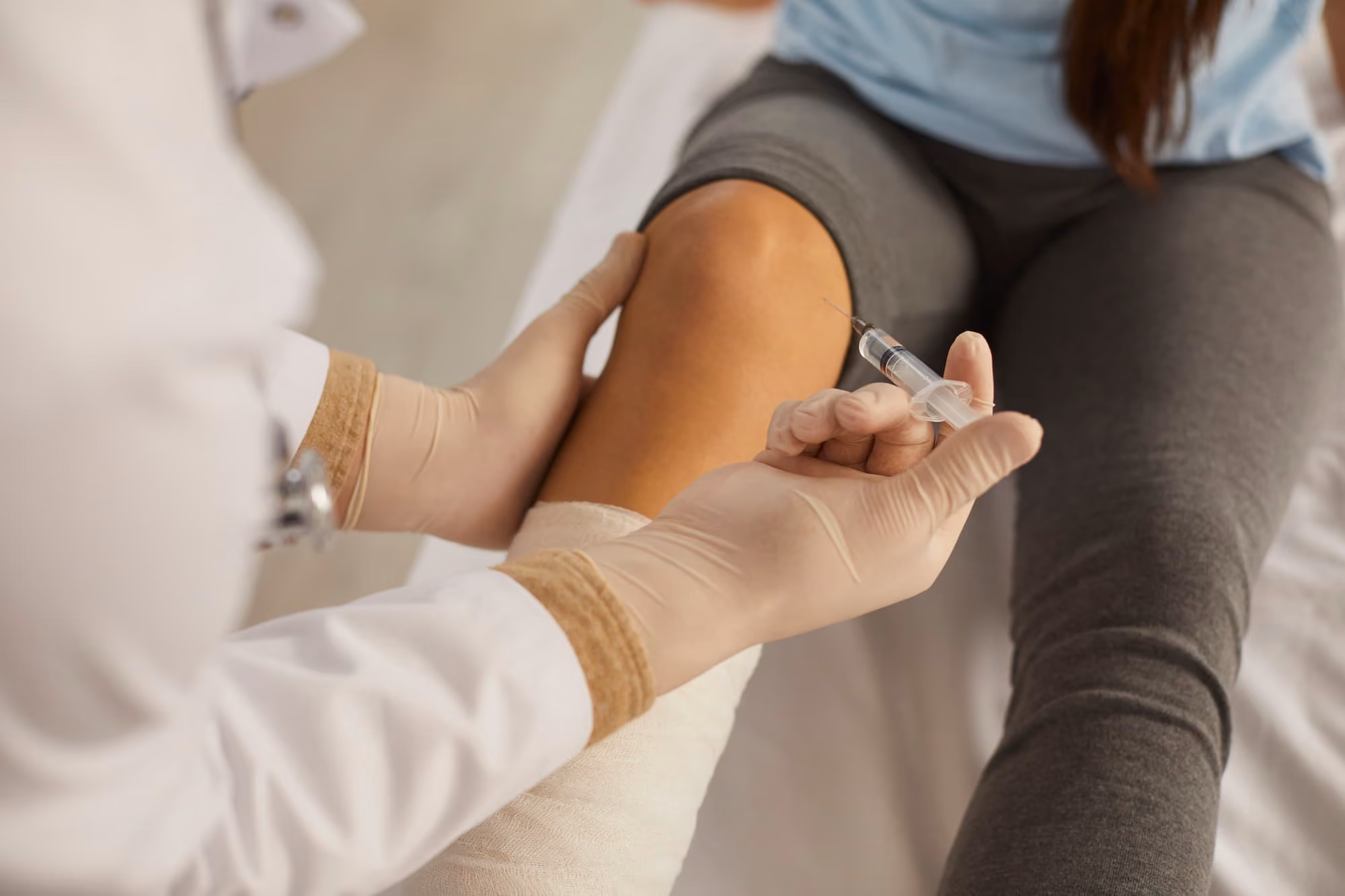 Medical professional wearing gloves preparing to inject a syringe into a person's knee.