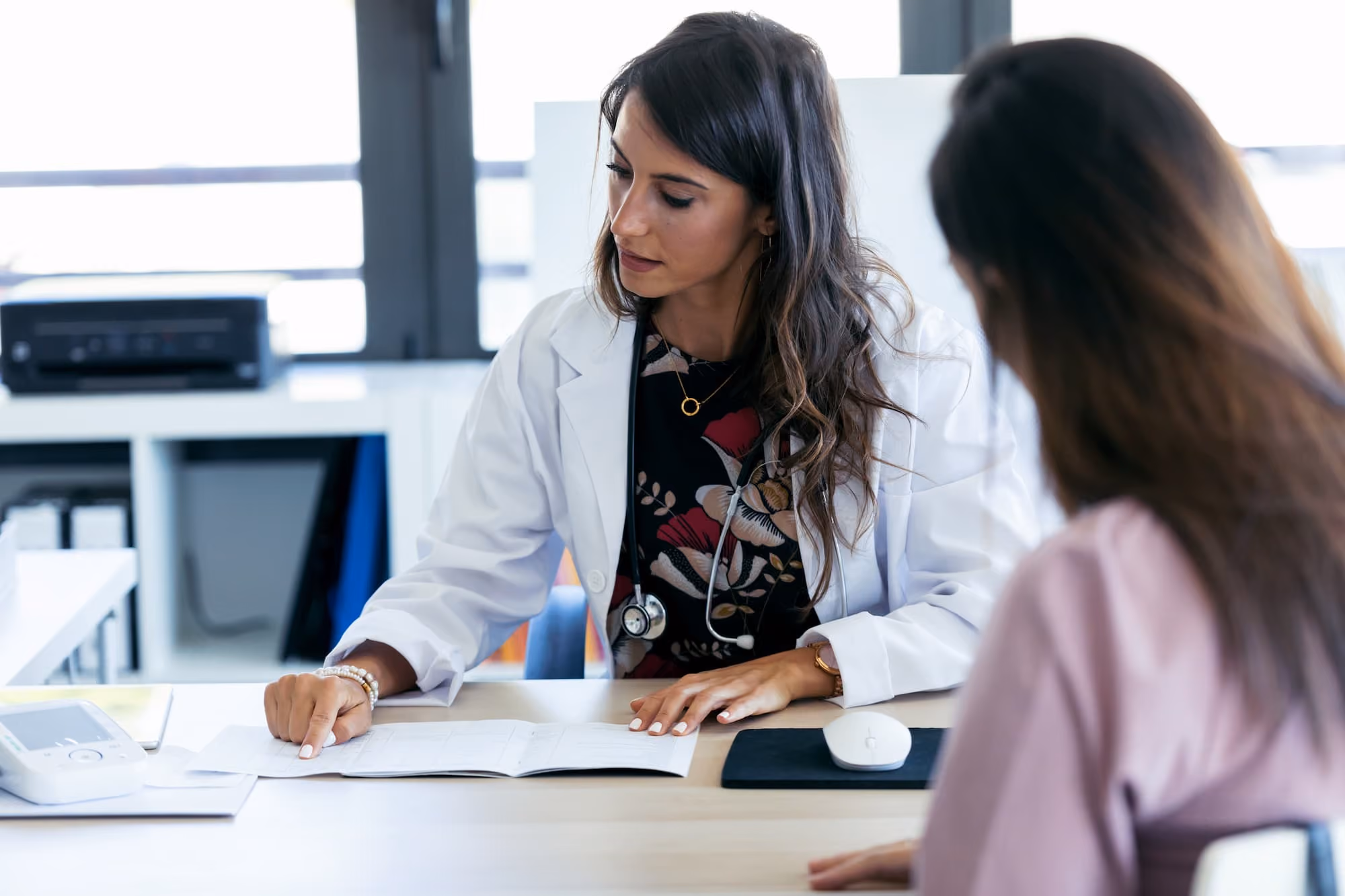 Female doctor in white coat explaining medical documents to patient across the desk.