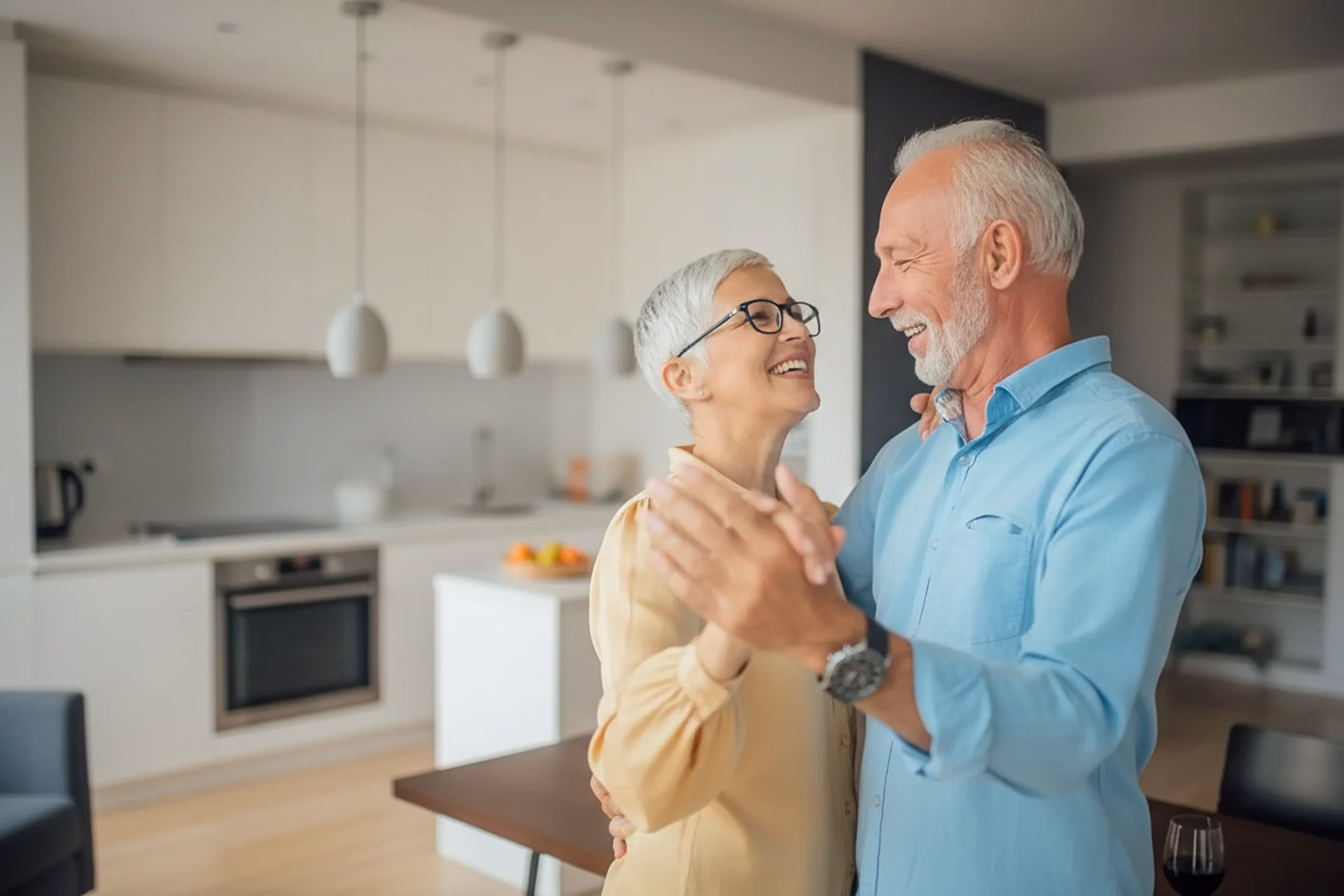 Smiling elderly couple dancing together in a modern kitchen.