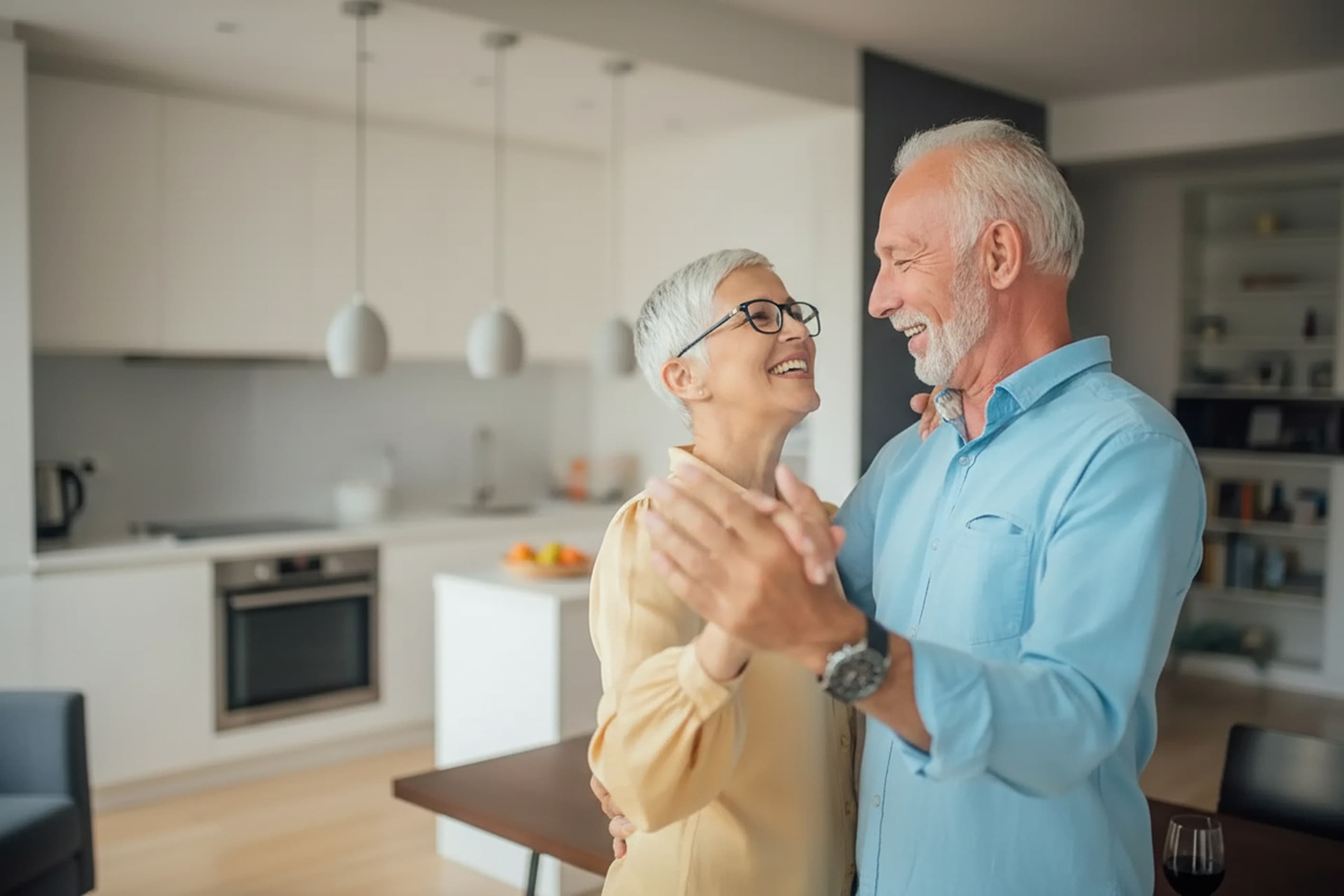 Smiling elderly couple dancing together in a modern kitchen.