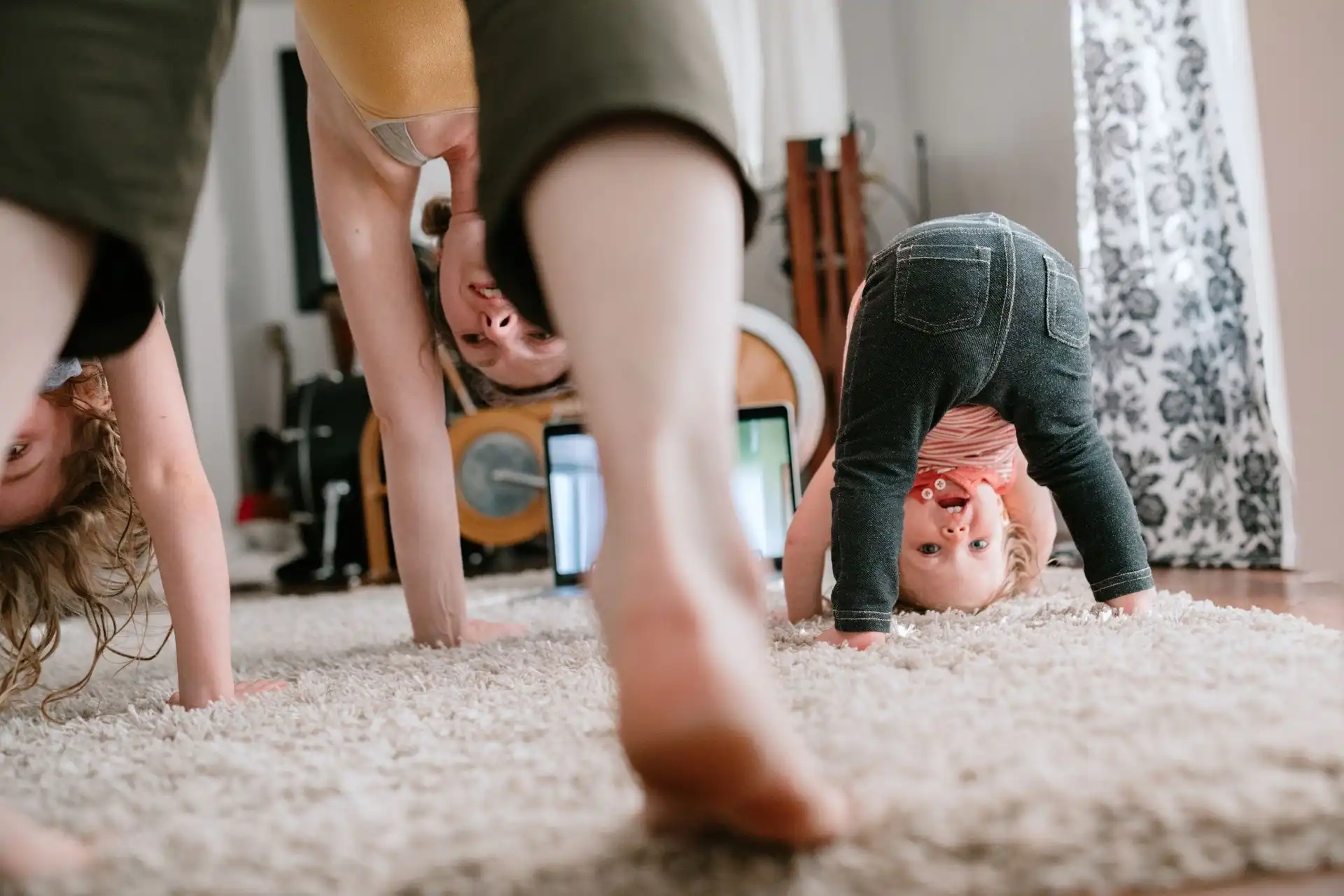 Family doing exercise together at home with a woman and child on a beige carpet.