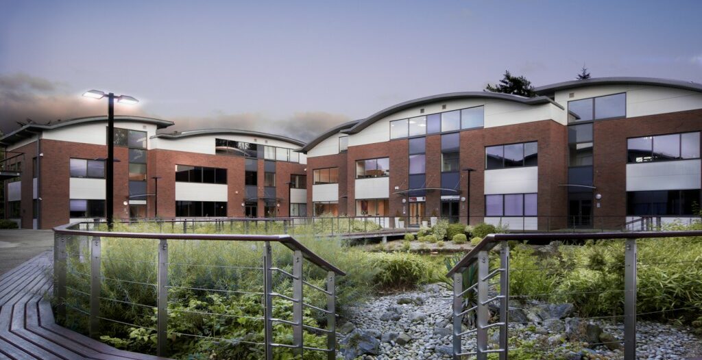 Modern brick office buildings with large windows surrounding a landscaped garden with a dry rock creek and metal railings.