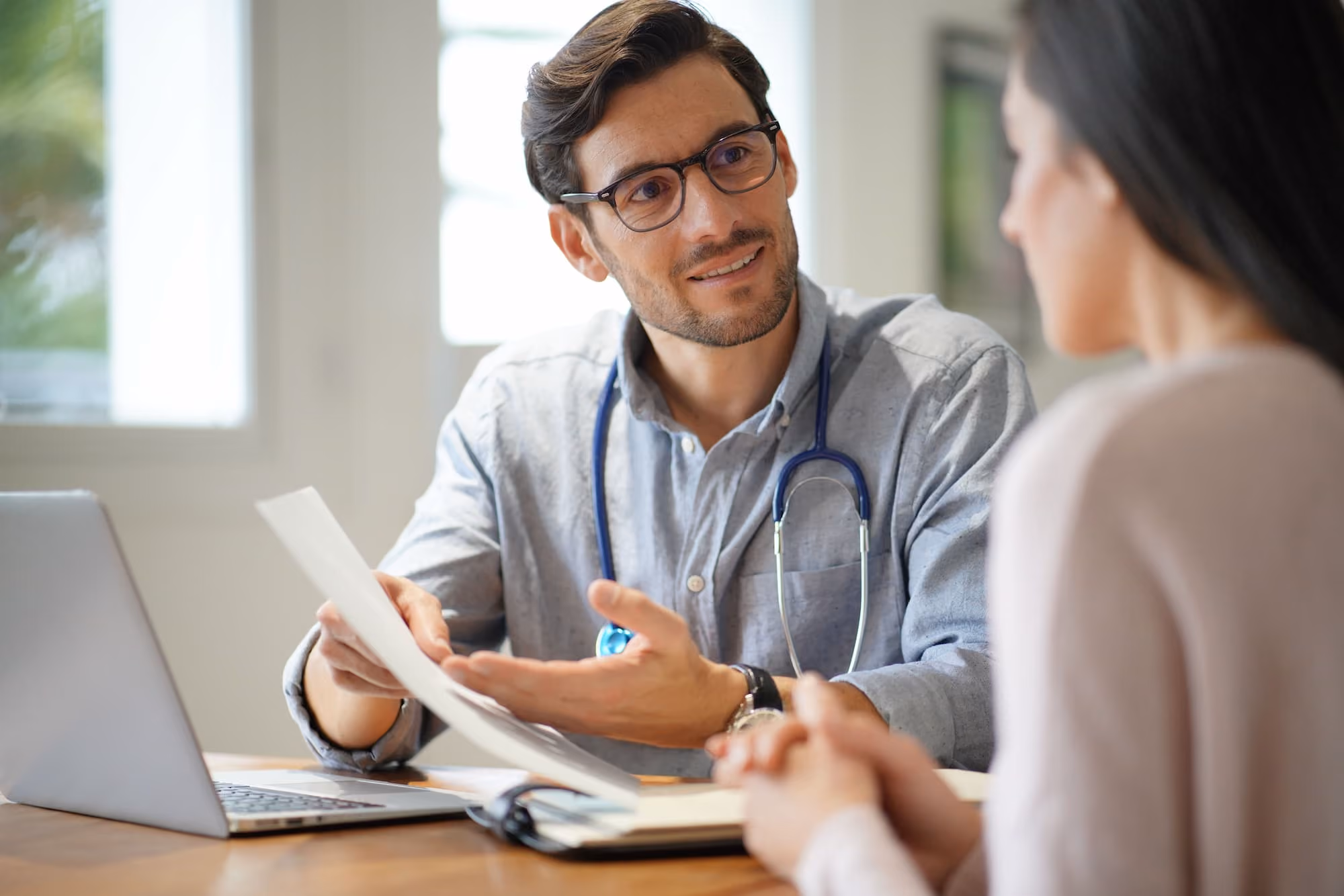 Male doctor with stethoscope around neck explaining medical information to female patient.