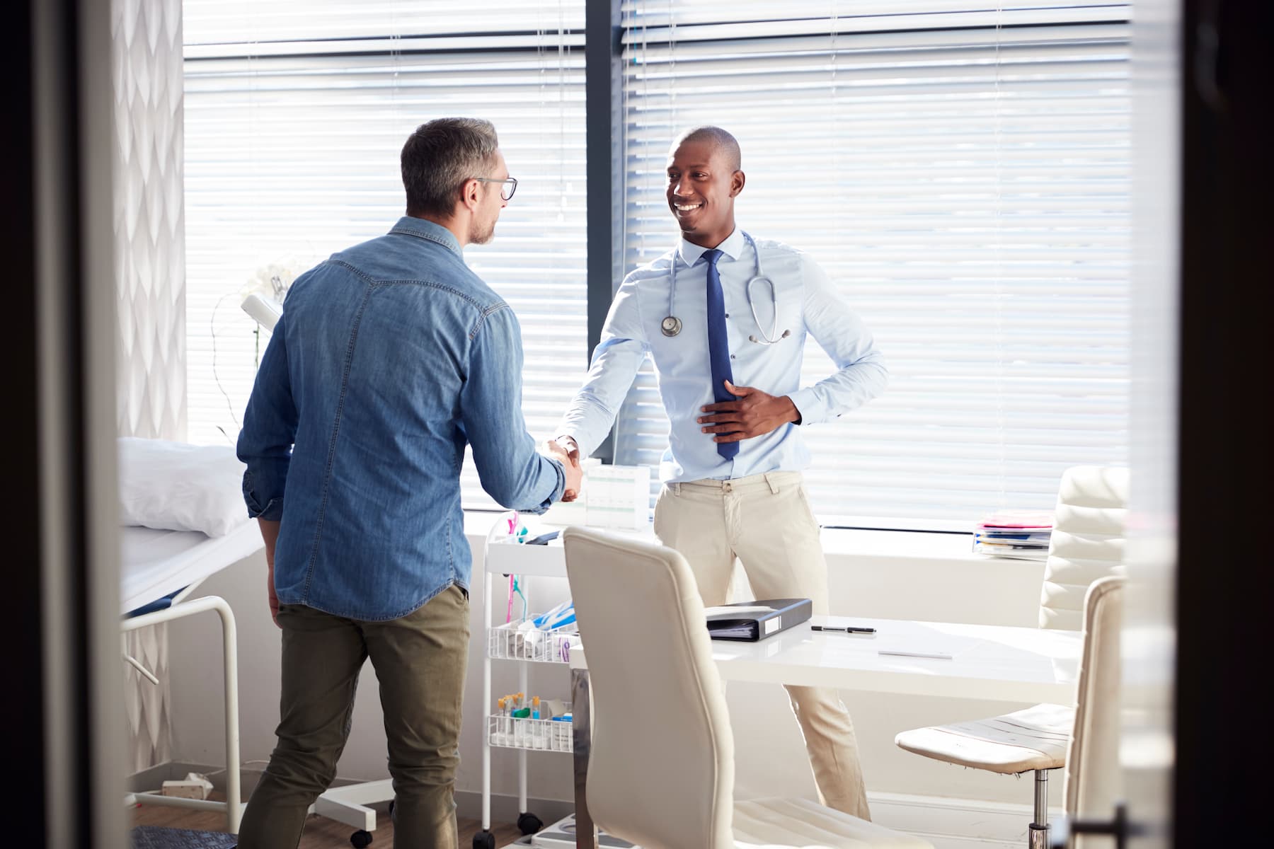 Doctor with stethoscope shaking hands with a patient in a bright medical office.
