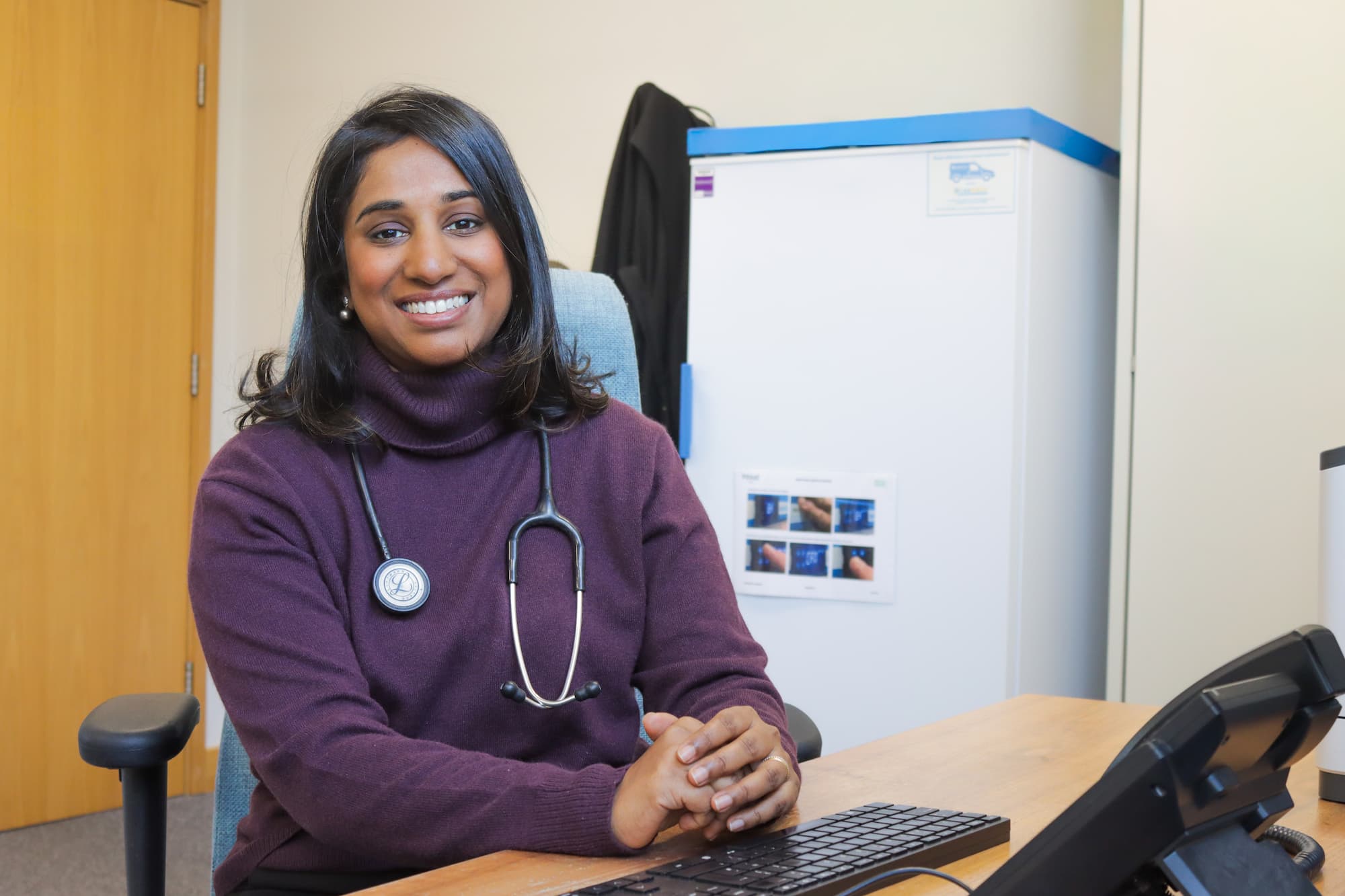 Smiling female doctor with a stethoscope sitting at a desk in an office.