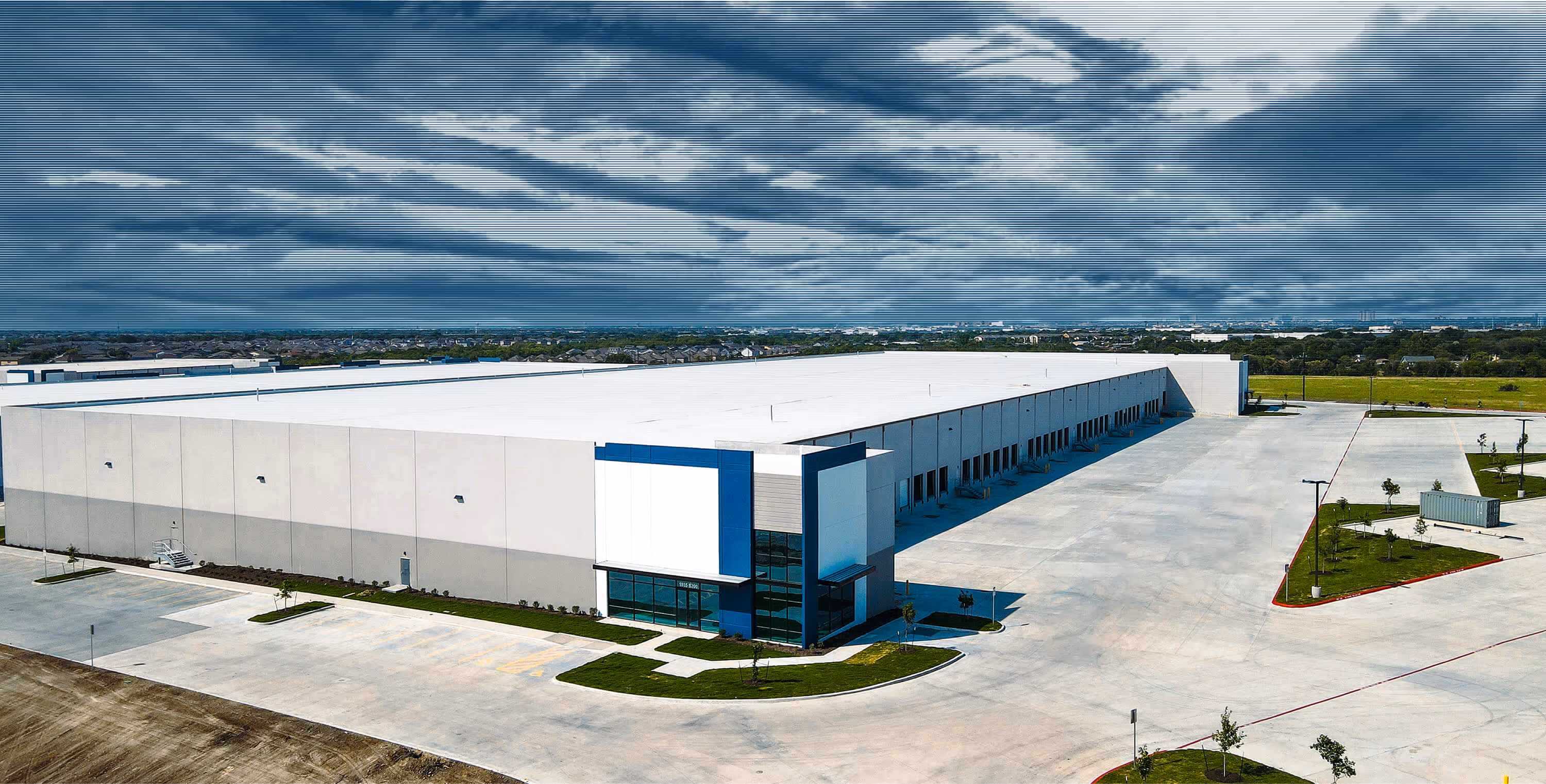 Large modern industrial warehouse with multiple loading docks under a cloudy sky.