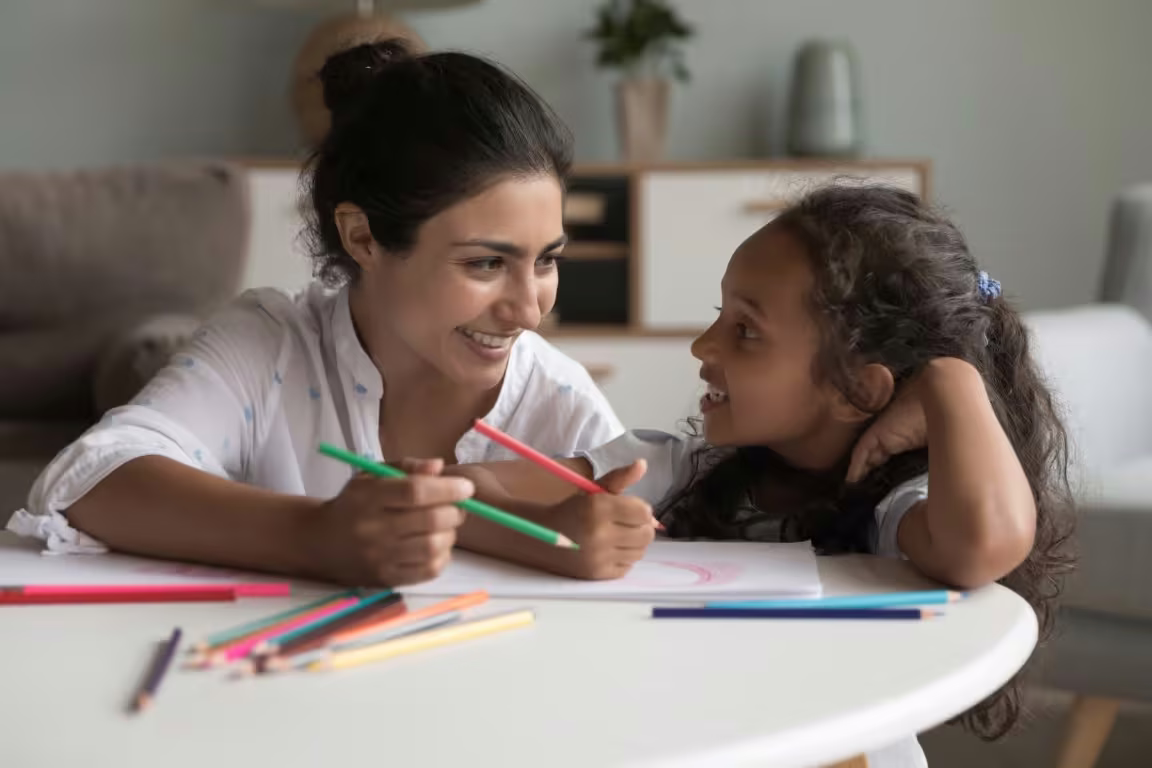 A woman and a young girl drawing together with coloured pencils at a table at home