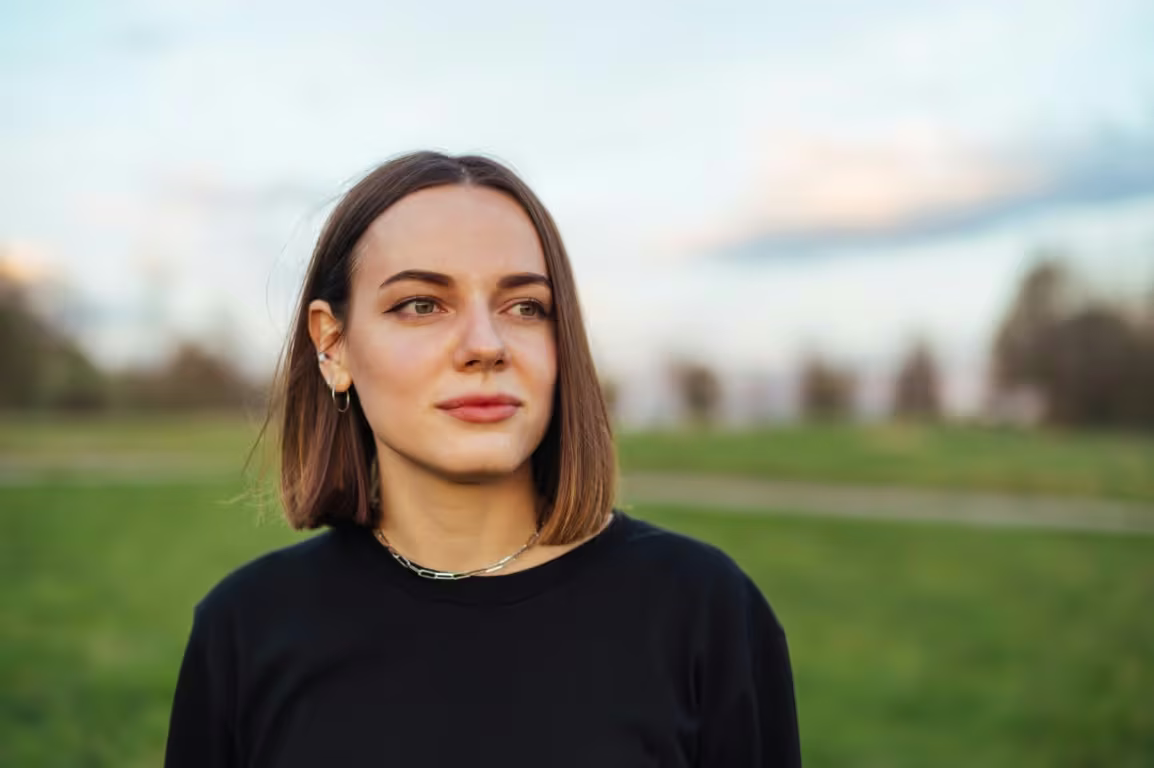 A young woman standing in a park, looking thoughtfully into the distance