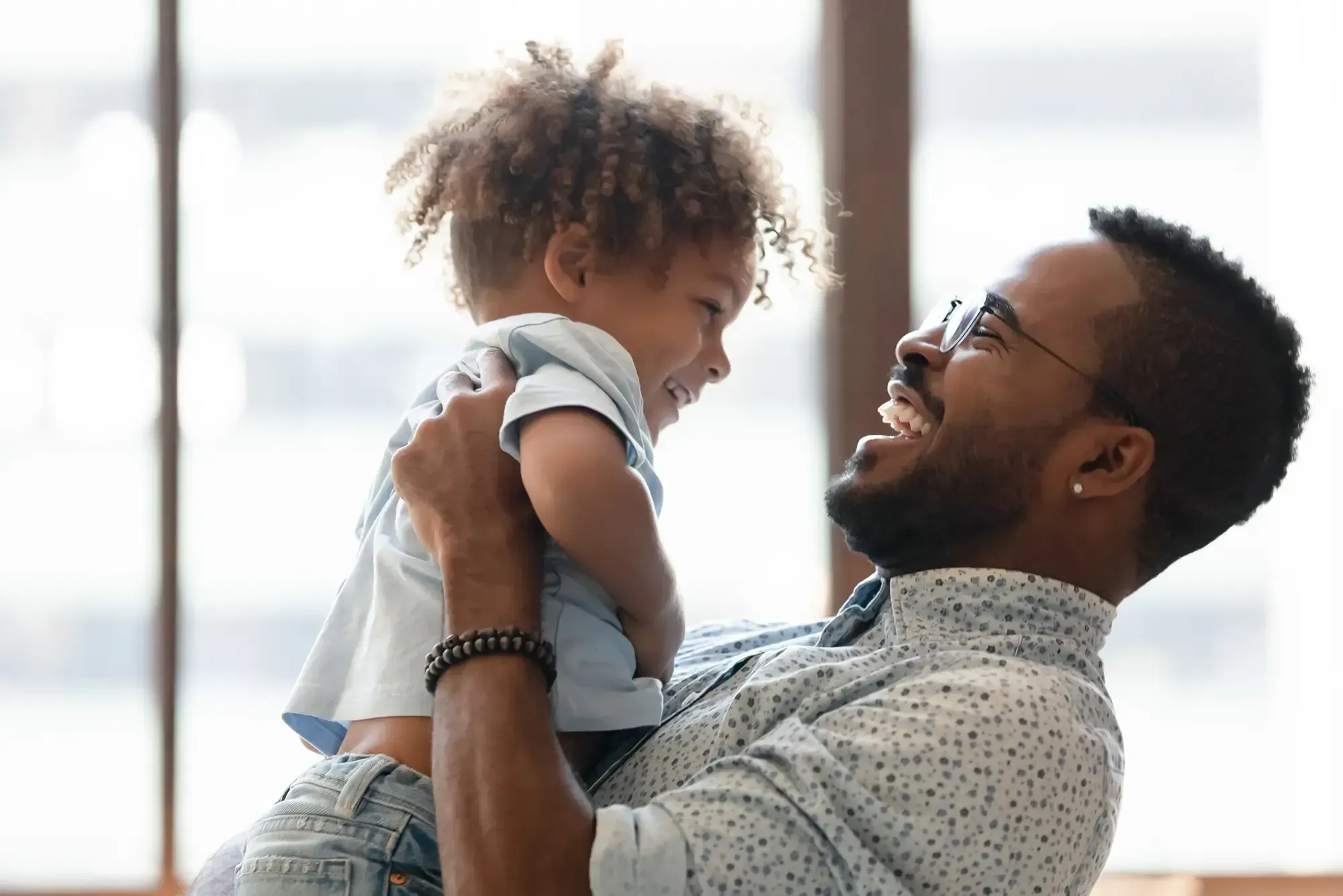 A father laughing joyfully as he holds up his smiling toddler