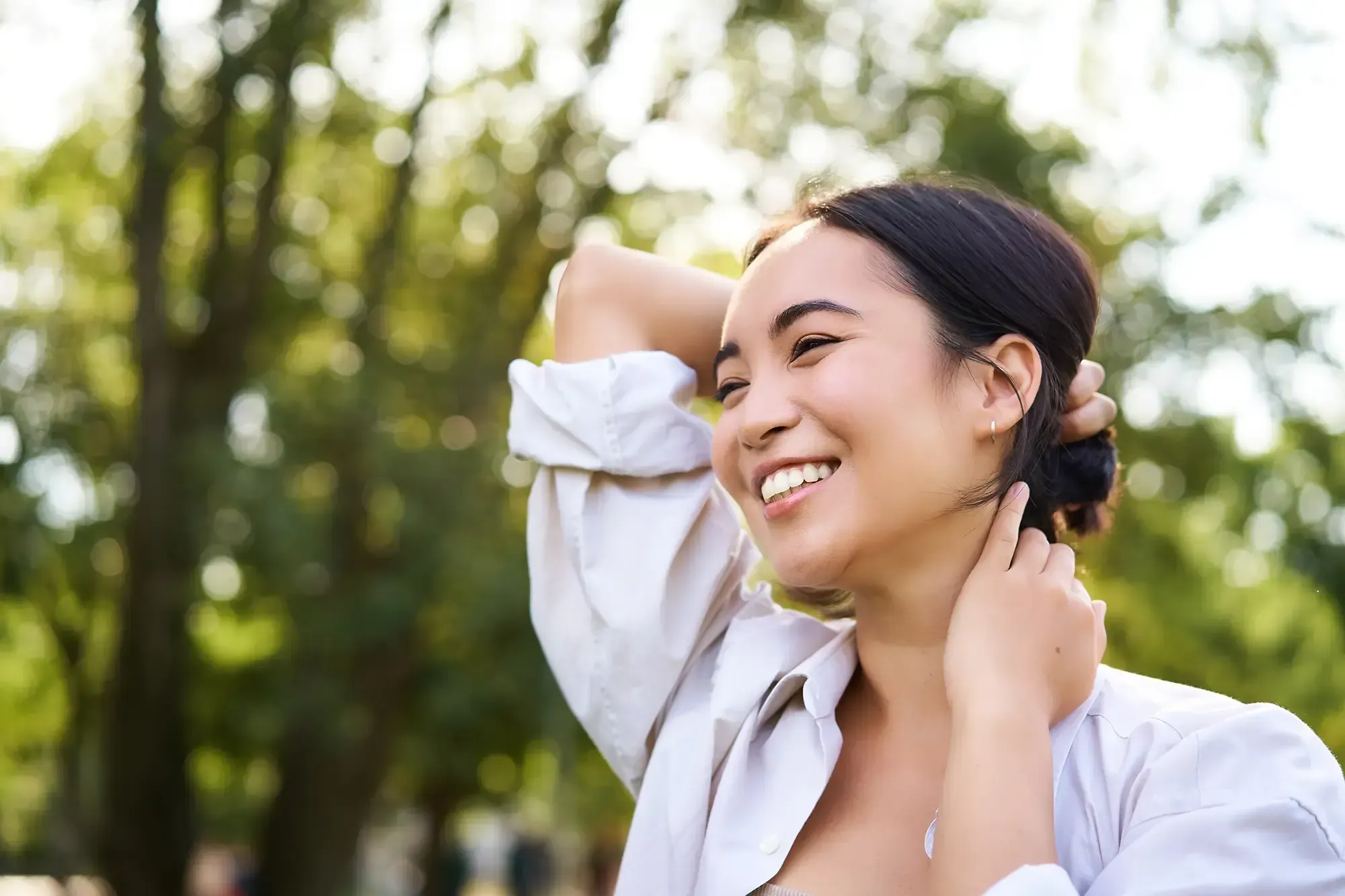 A young woman smiling contentedly outdoors, surrounded by lush green trees