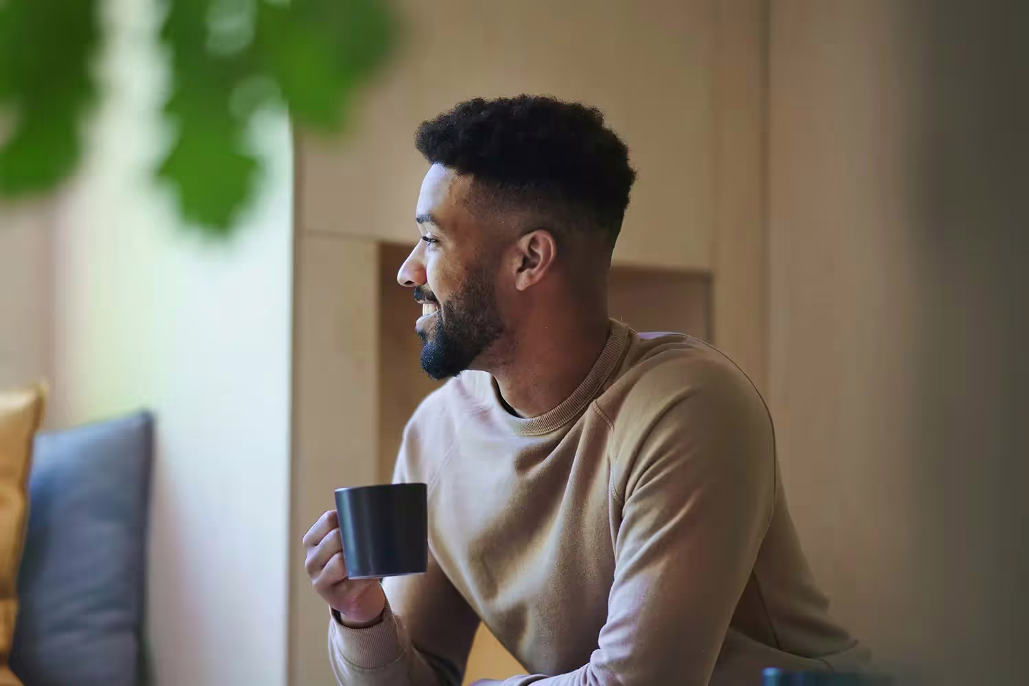 A man sitting with a coffee mug, smiling and looking out of a window