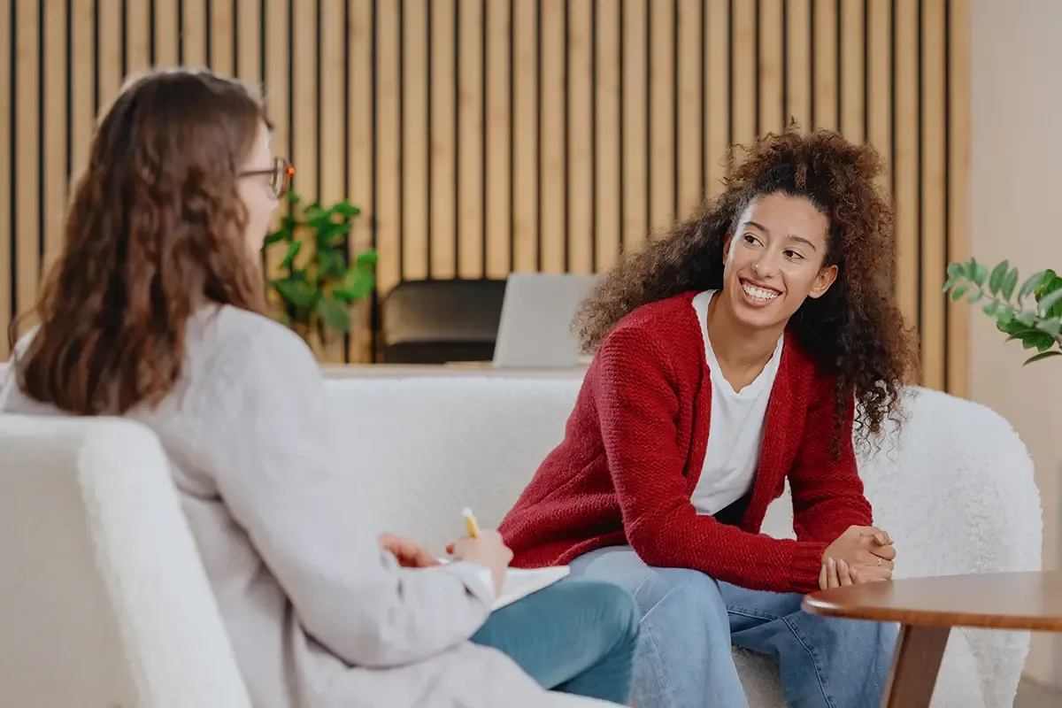 Two women sitting on a couch engaged in a friendly conversation in a modern room.
