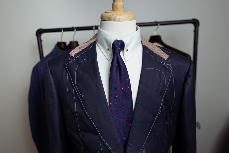 Baste-stage navy suit jacket with white stitching on a dress form