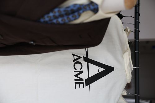 Brown suit on mannequin next to a garment bag with a black ACME logo on a white background.