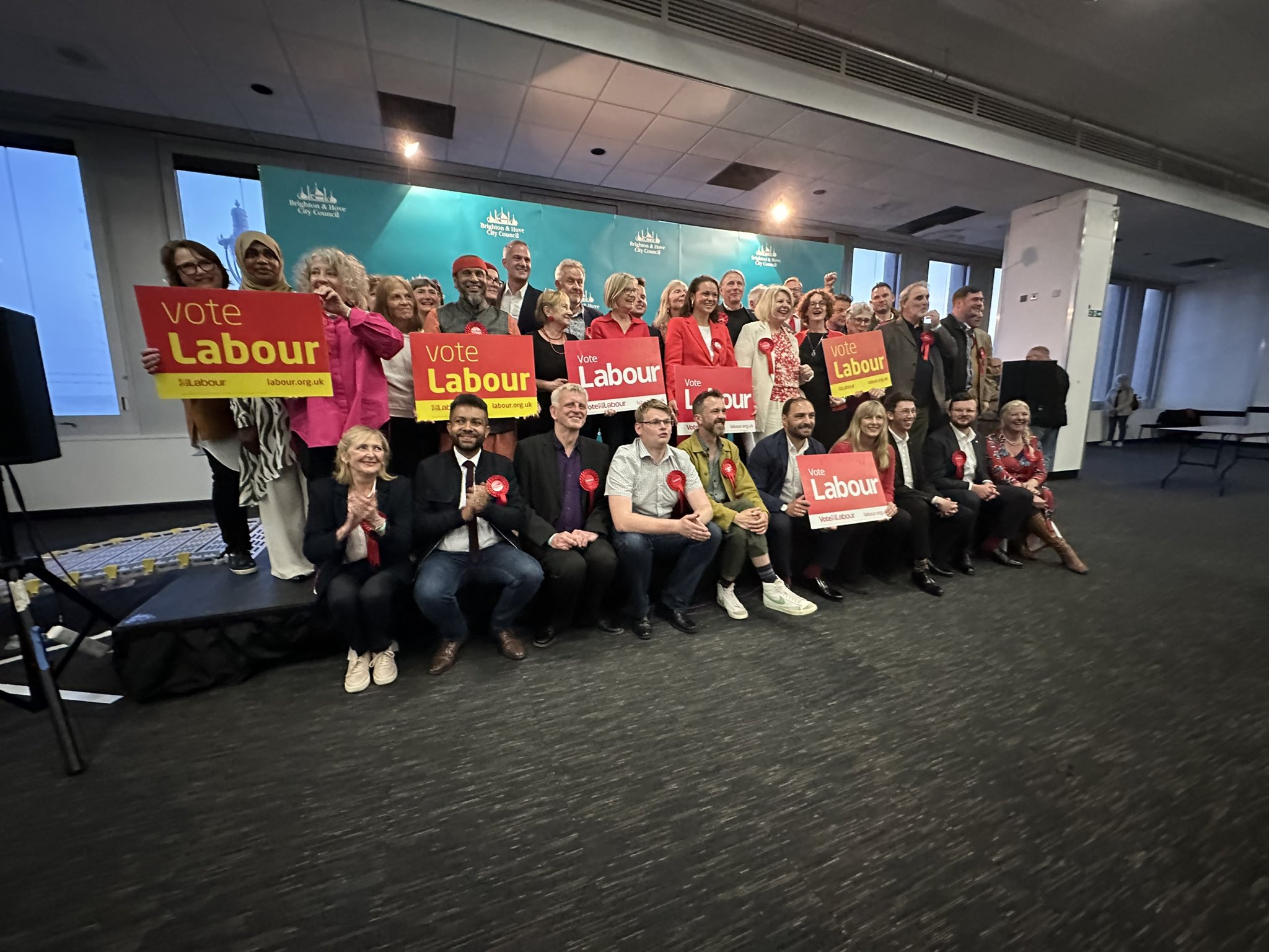 Group newly elected coucillors, including Leslie, posing indoors holding and displaying red and yellow 'Vote Labour' signs, in front of a Brighton & Hove City Council backdrop.