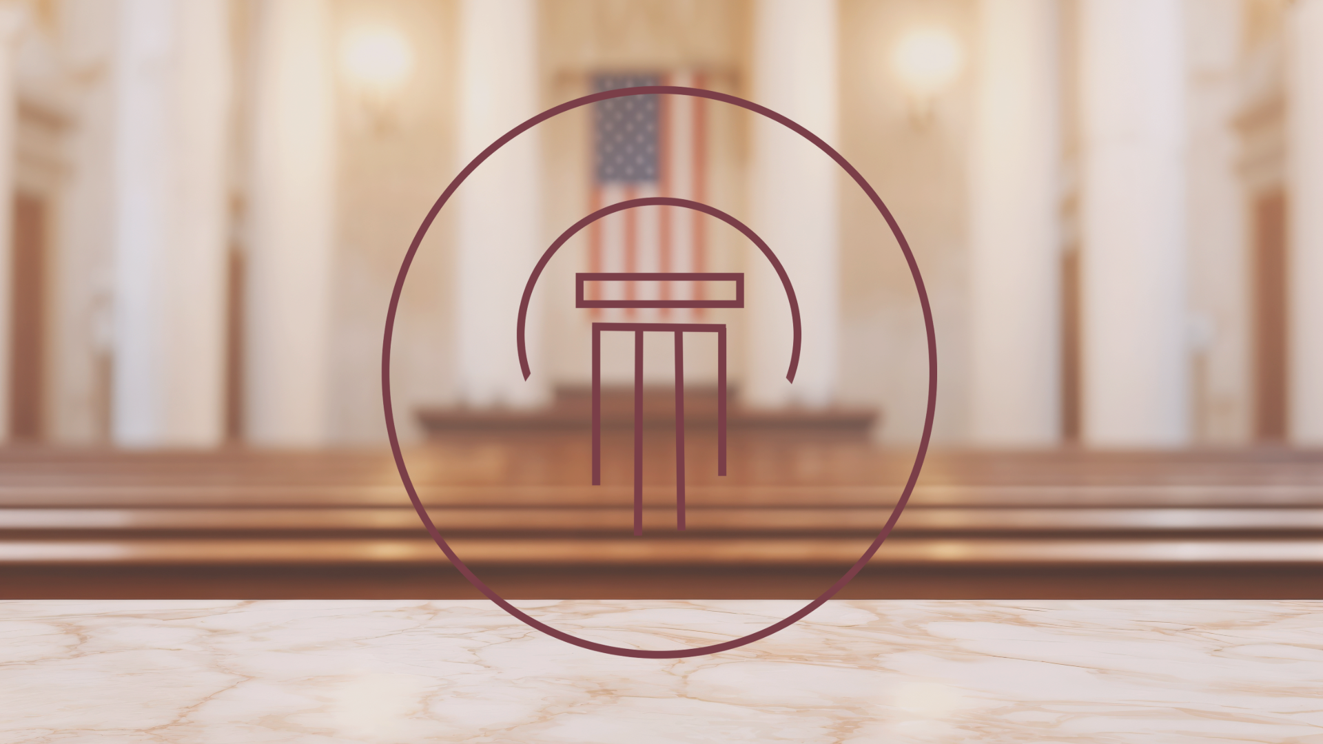 Wooden benches in a courtroom with a blurred American flag and judge's bench in the background.