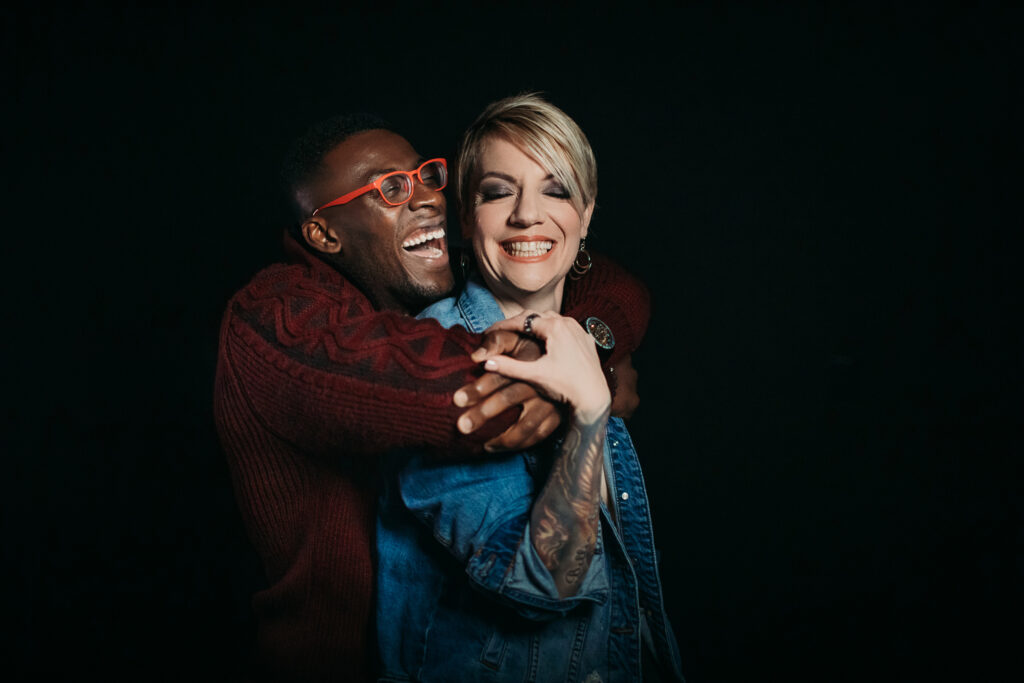 Couple celebrating their relationship with laughter and love through photography against a black backdrop. Photography by Lindsay Hite