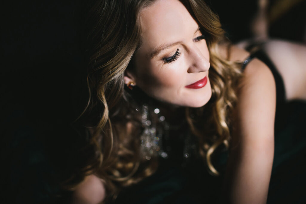 Woman in black bra on belly with a black background.  Boudoir photography by Lindsay Hite