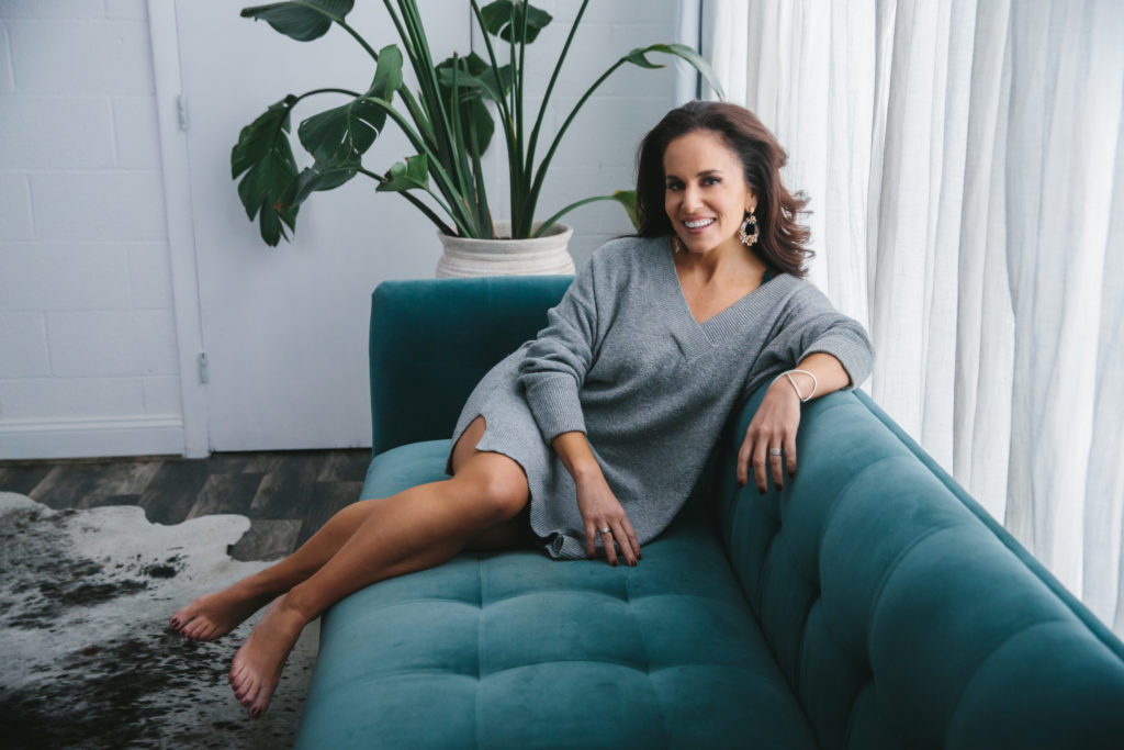 woman in oversized sweater on teal sofa; photography by Lindsay Hite