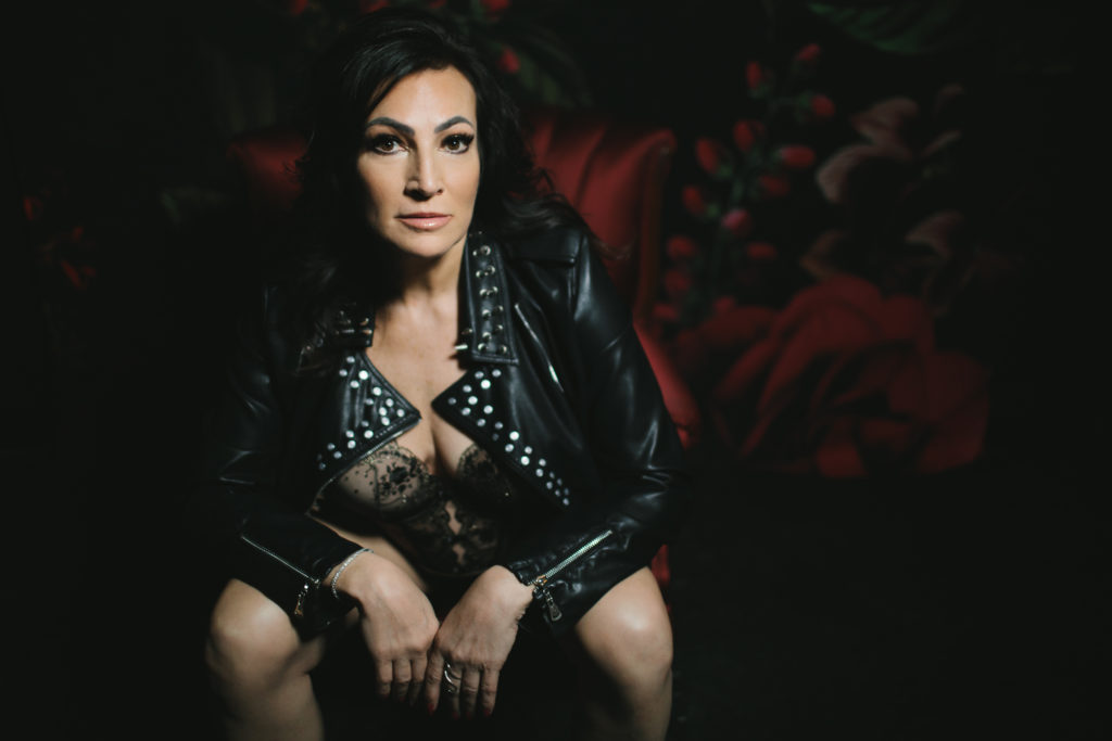 Woman in body suit and leather jacket with dark floral background, photography by Lindsay Hite