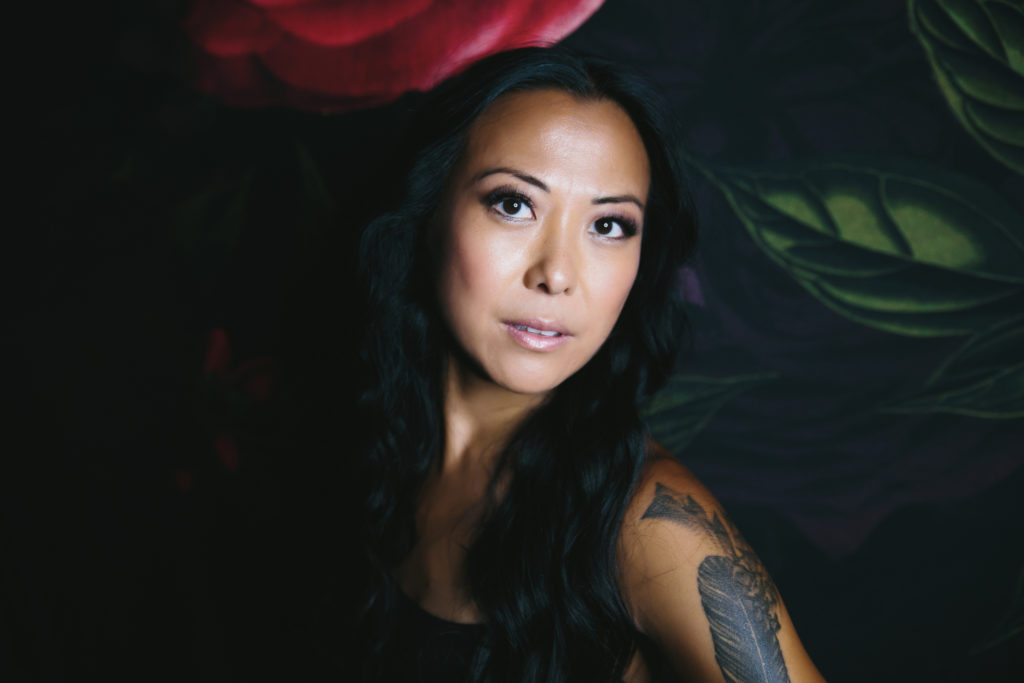Asian woman smiling while seated in front of rose backdrop, photography by Lindsay Hite