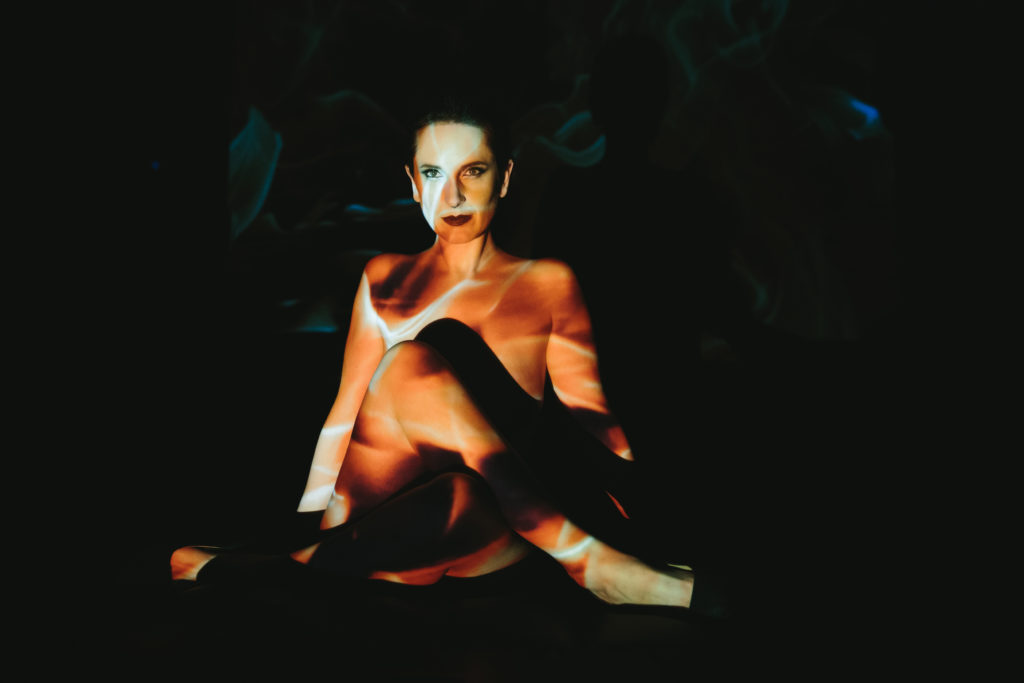 Woman sitting cross legged with a black background and a golden image projected over her. 