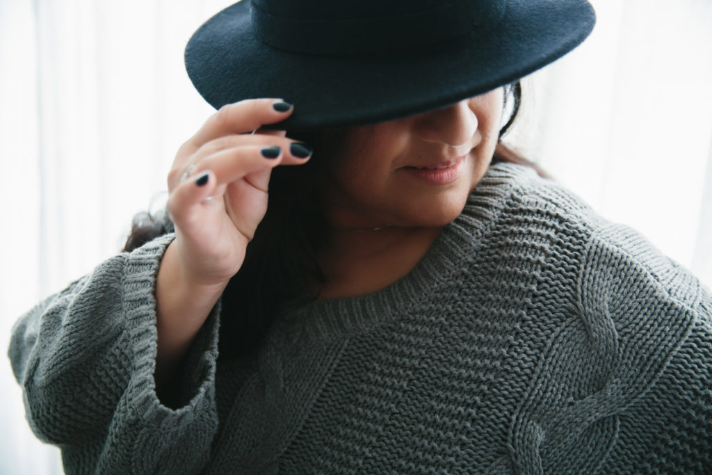 Woman in sweater and black at with a white curtain background; photography by Lindsay Hite